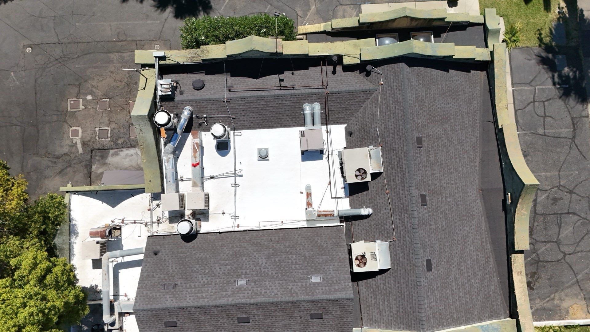 Aerial view of a flat rooftop with HVAC units, vents, and surrounding pavement and fencing