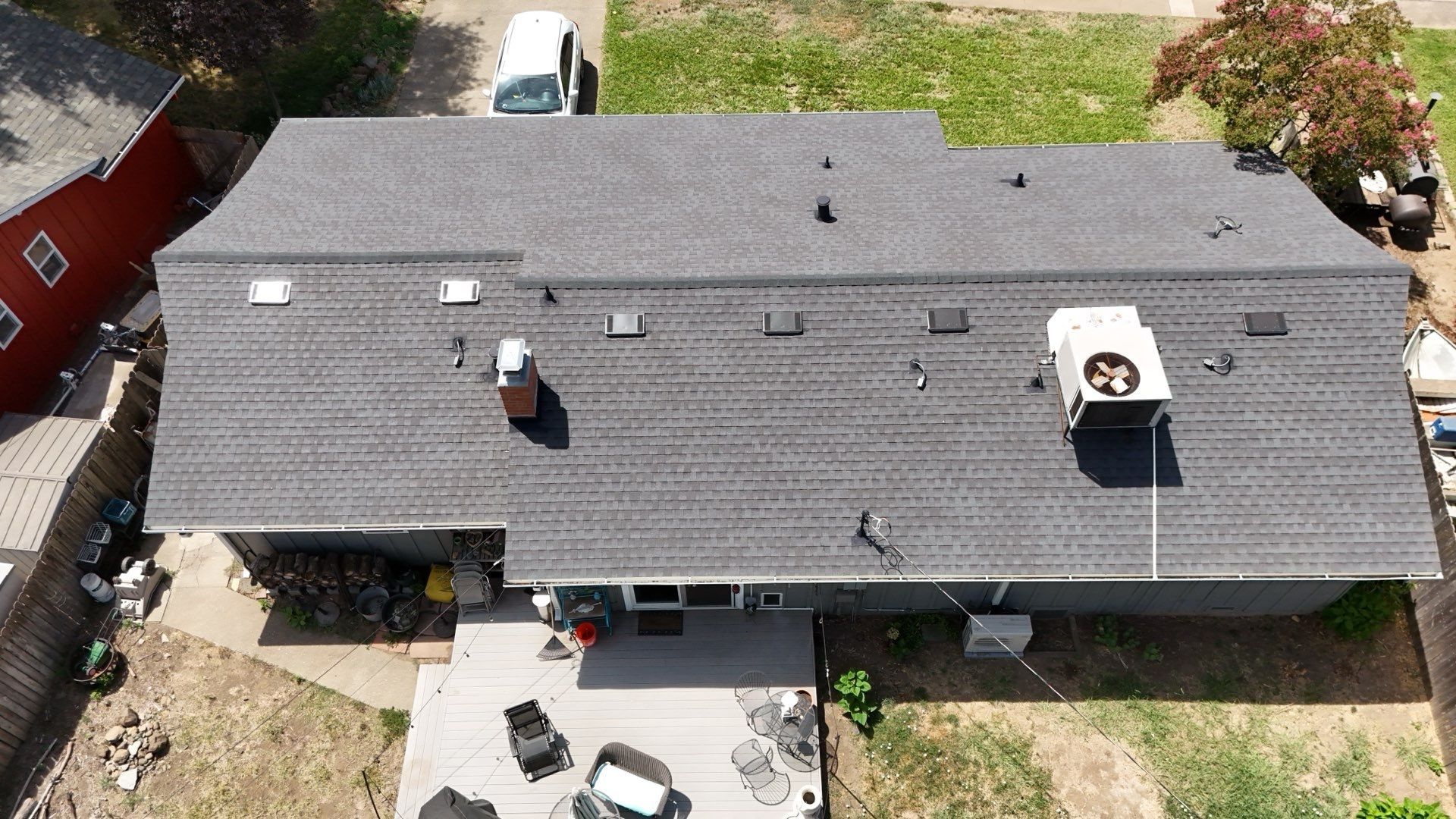 Aerial view of a house with a dark roof, rooftop vents, and a backyard patio.