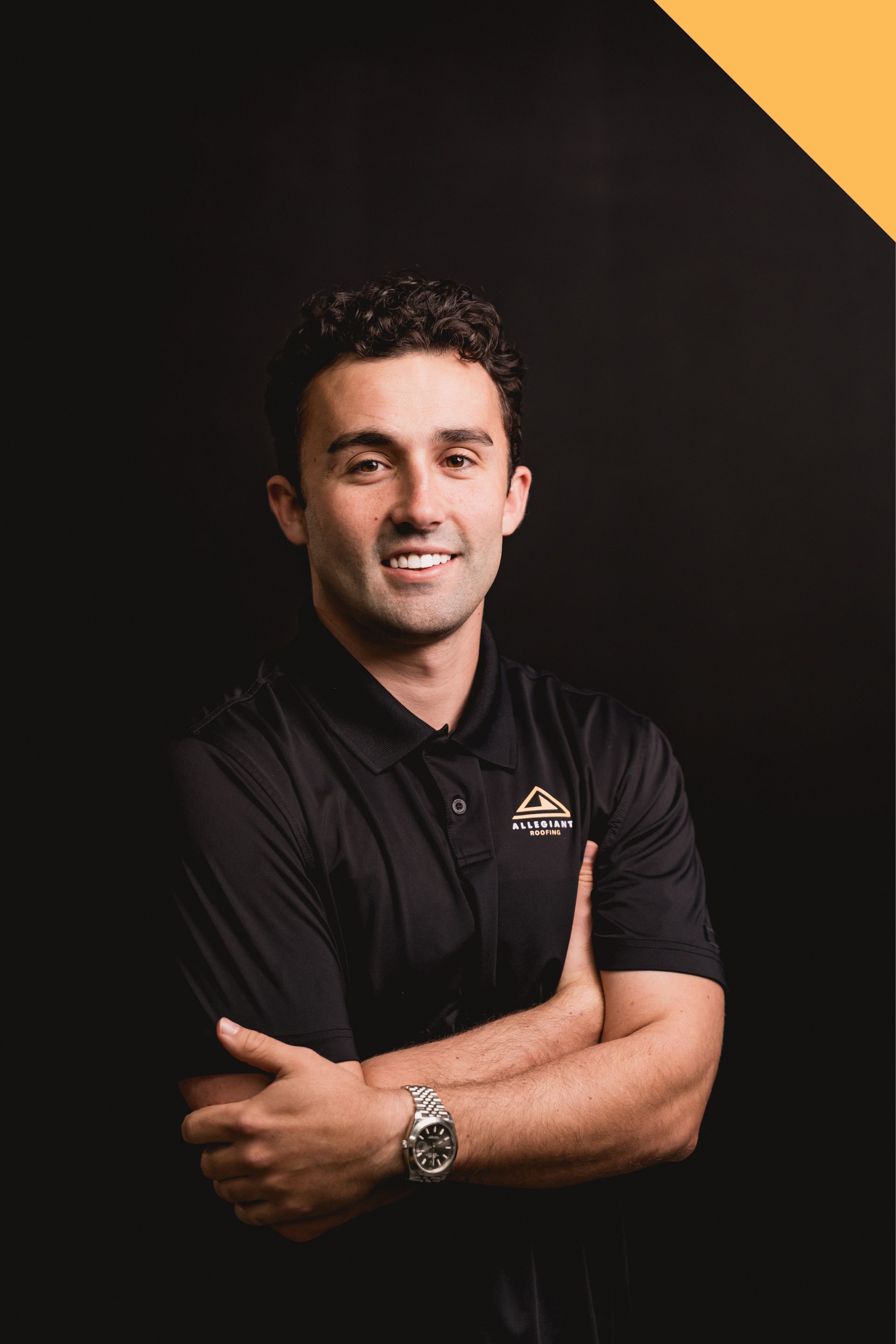 Portrait of a smiling person in a black polo shirt with arms crossed against a dark background