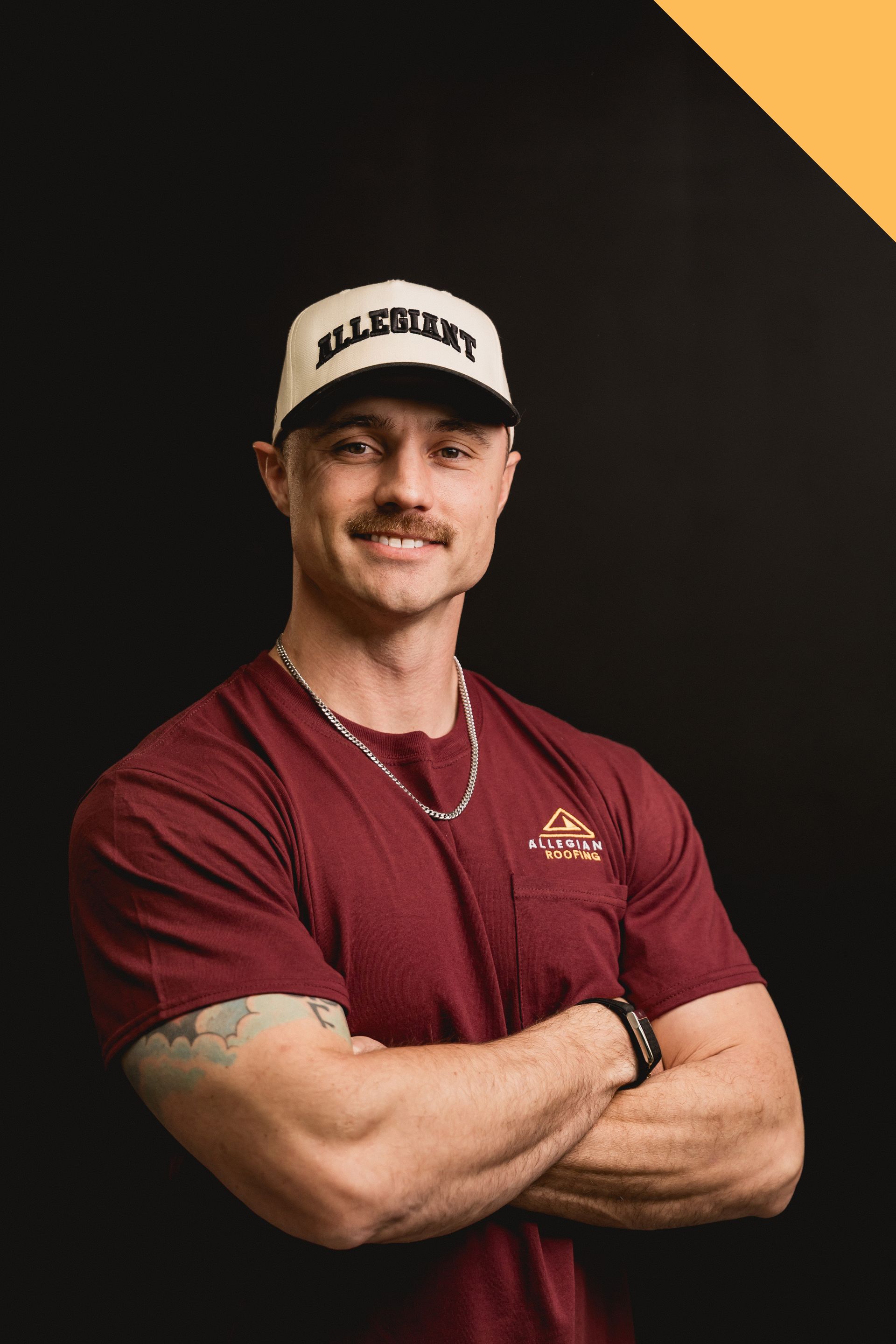Portrait of a smiling person with crossed arms, wearing a maroon shirt and white cap against a dark background