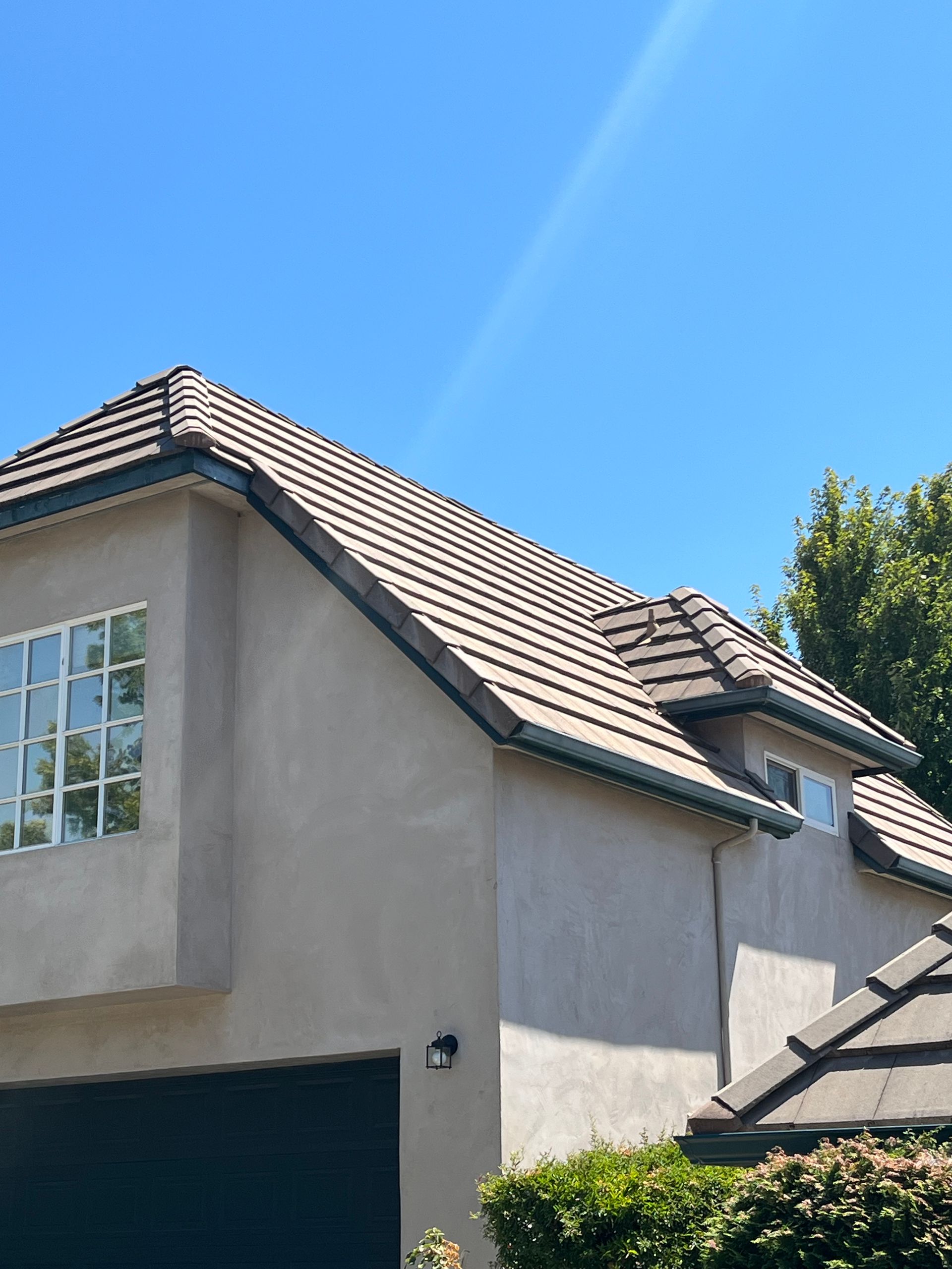 Suburban house exterior with gray stucco walls, tiled roof, garage, and bright blue sky