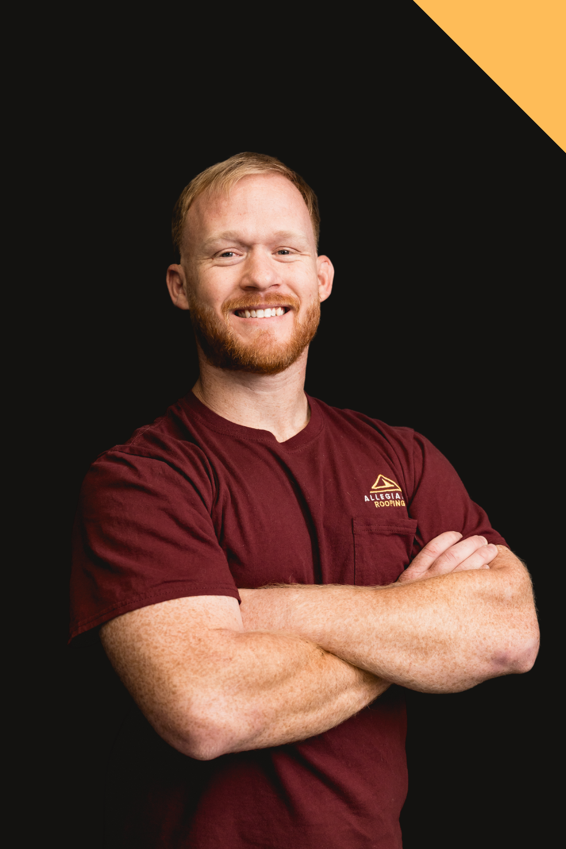 Man with folded arms in black shirt against dark background with gold corner accent