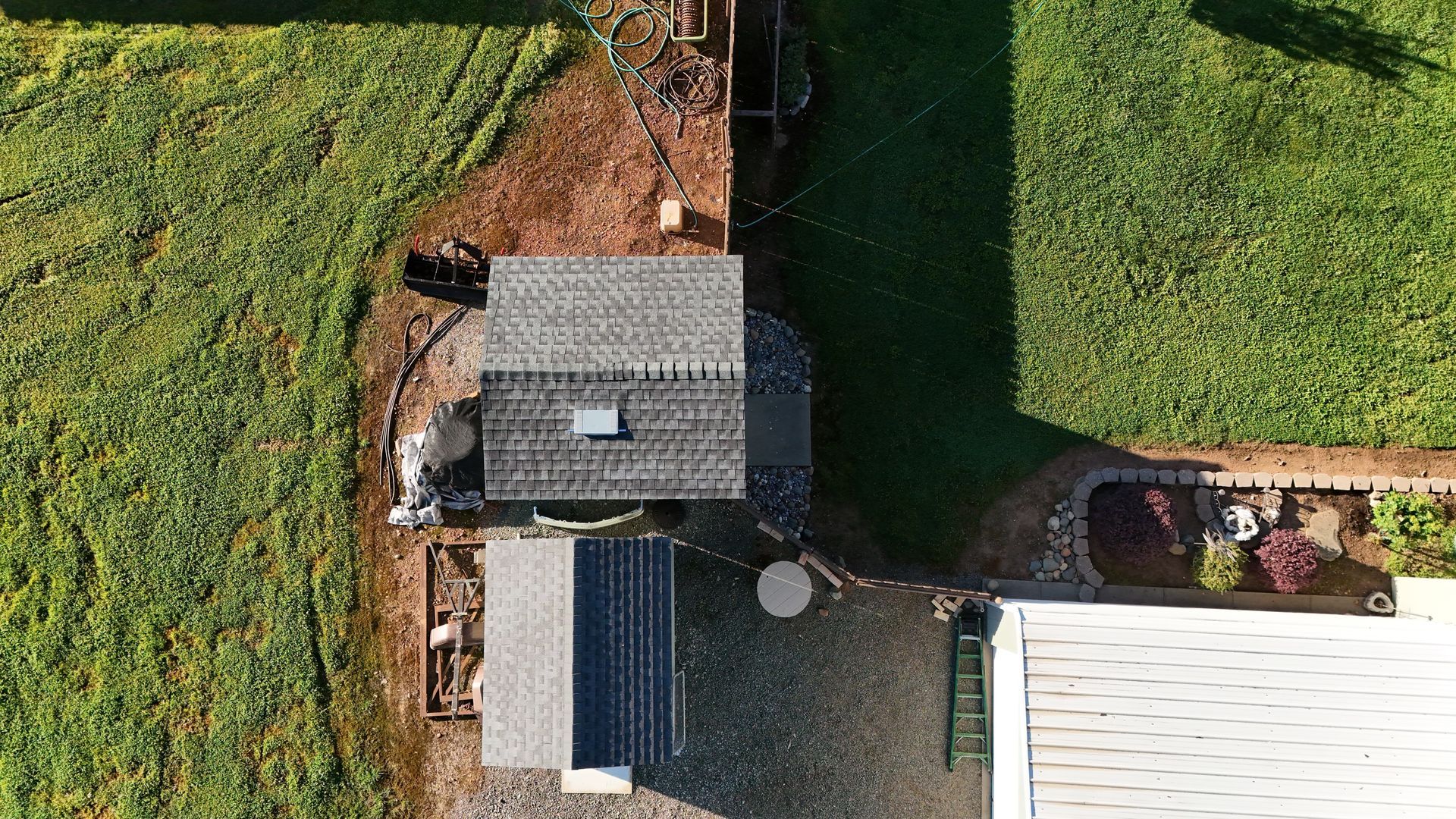 Aerial view of a small shed and adjacent house roof beside green fields and a garden path.