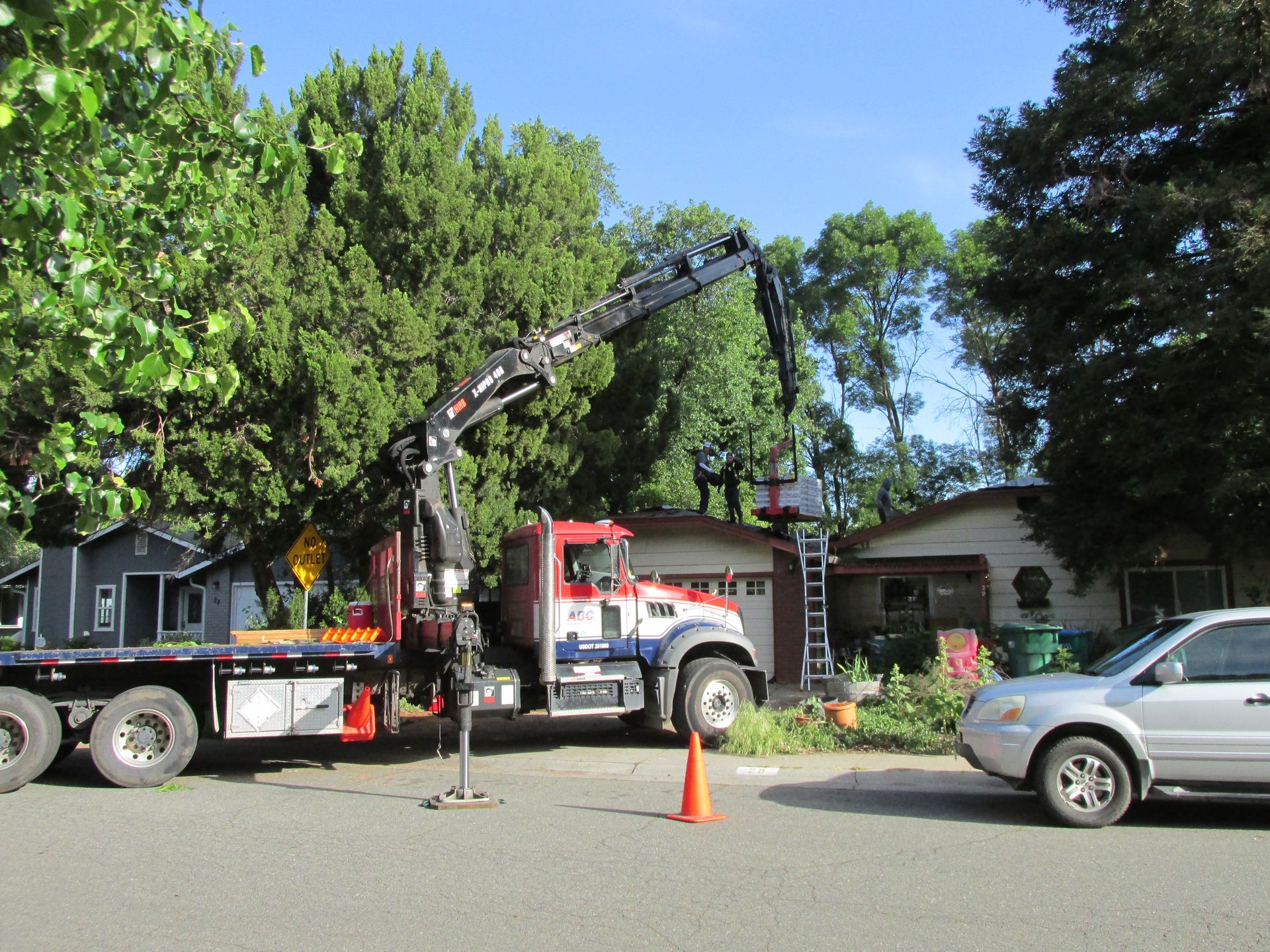 Tow truck with raised boom on a residential street beside a silver SUV and orange cone