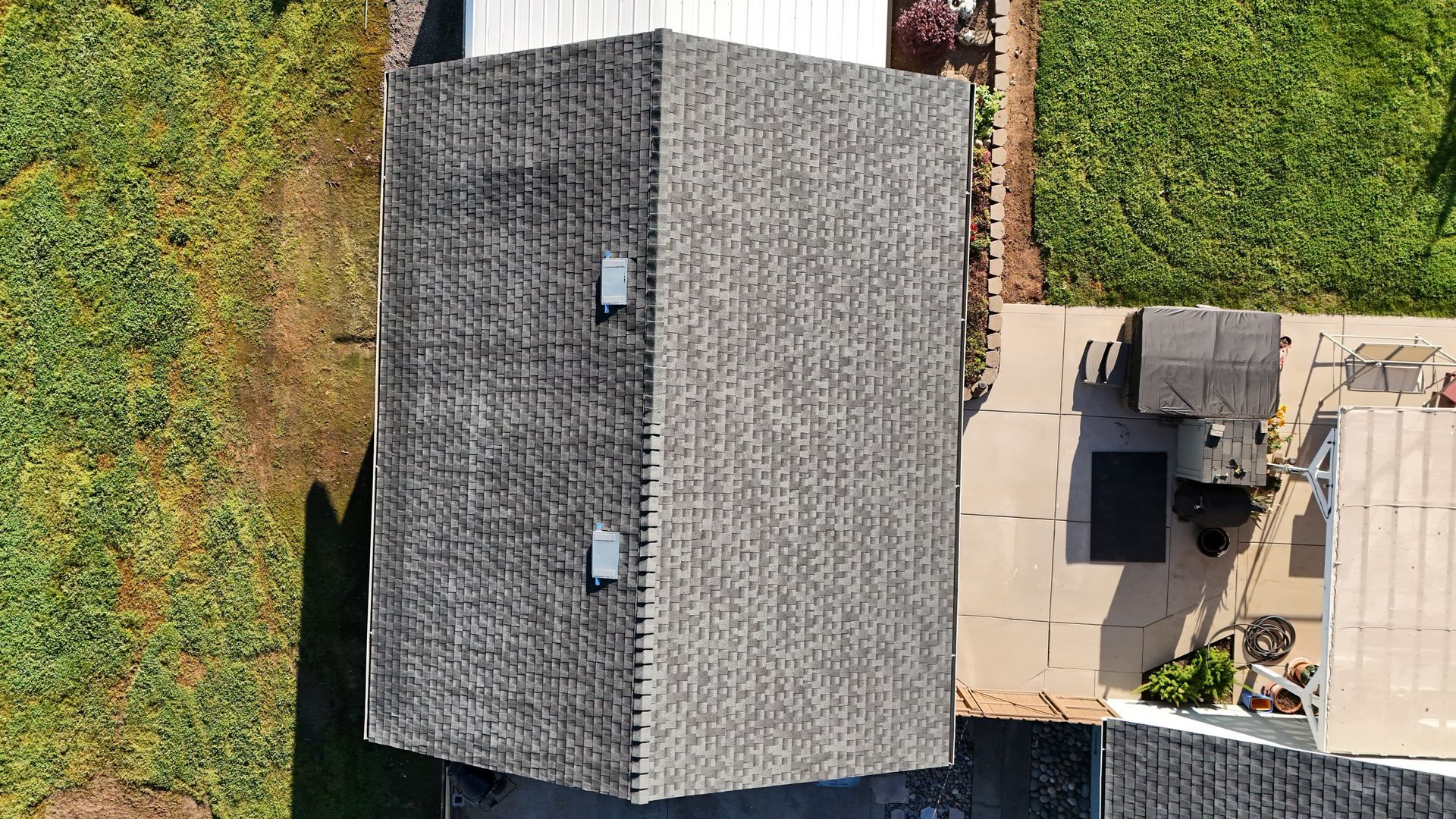 Aerial view of a gray-roofed house beside a patio and grassy yard.