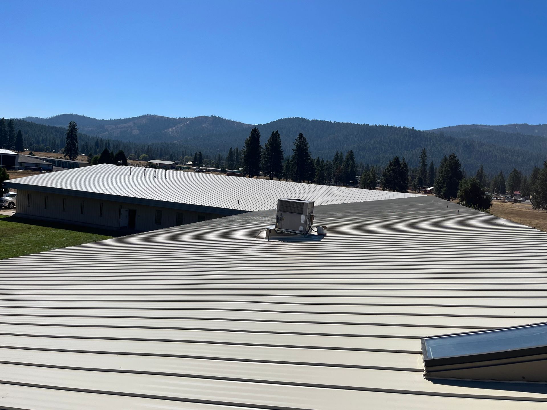 Rooftop with white metal panels and HVAC unit, overlooking trees and mountains under a clear blue sky