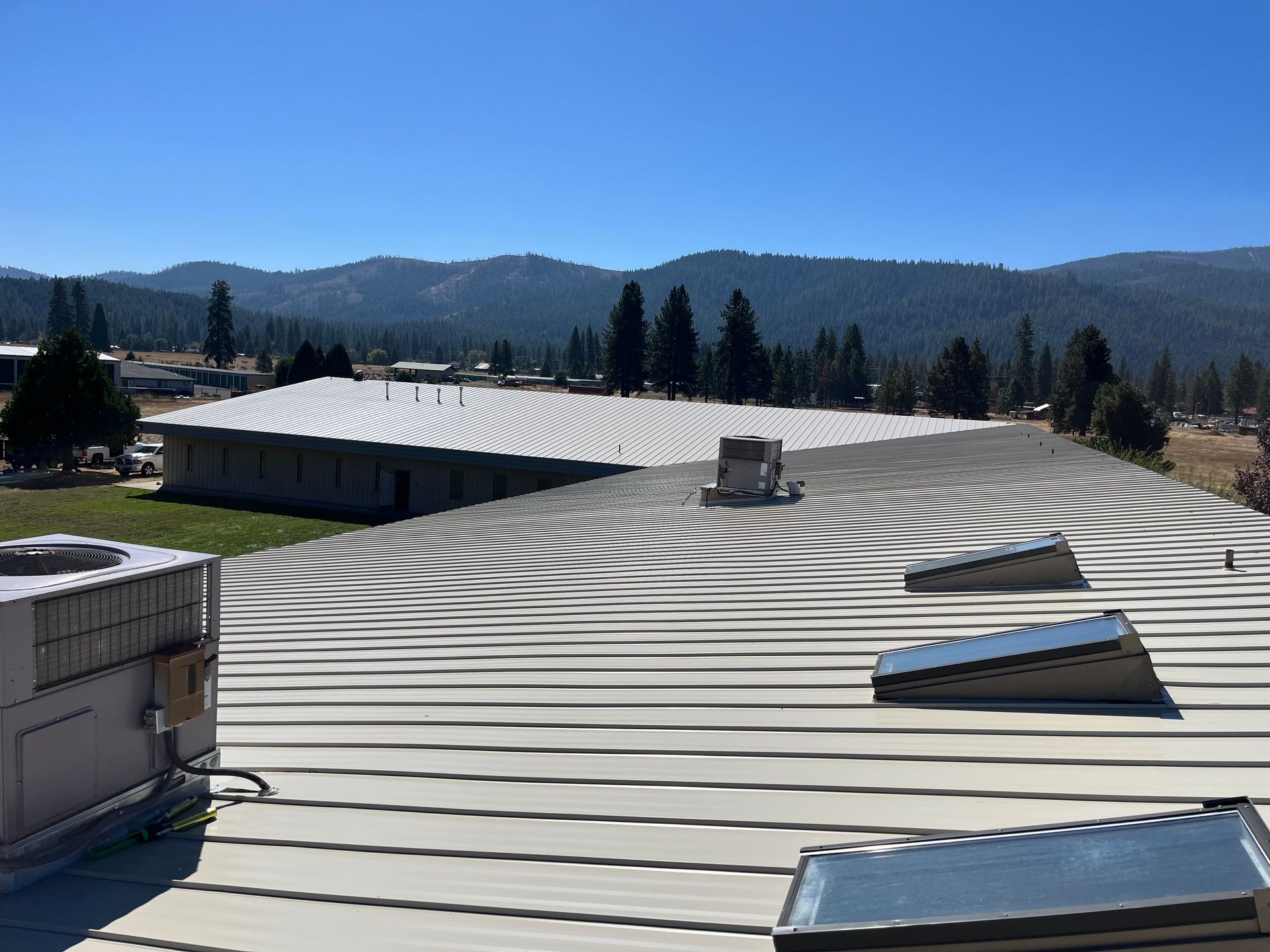 Rooftop with snow and repeating shadow stripes, with skylights under a clear blue sky and mountains in the distance