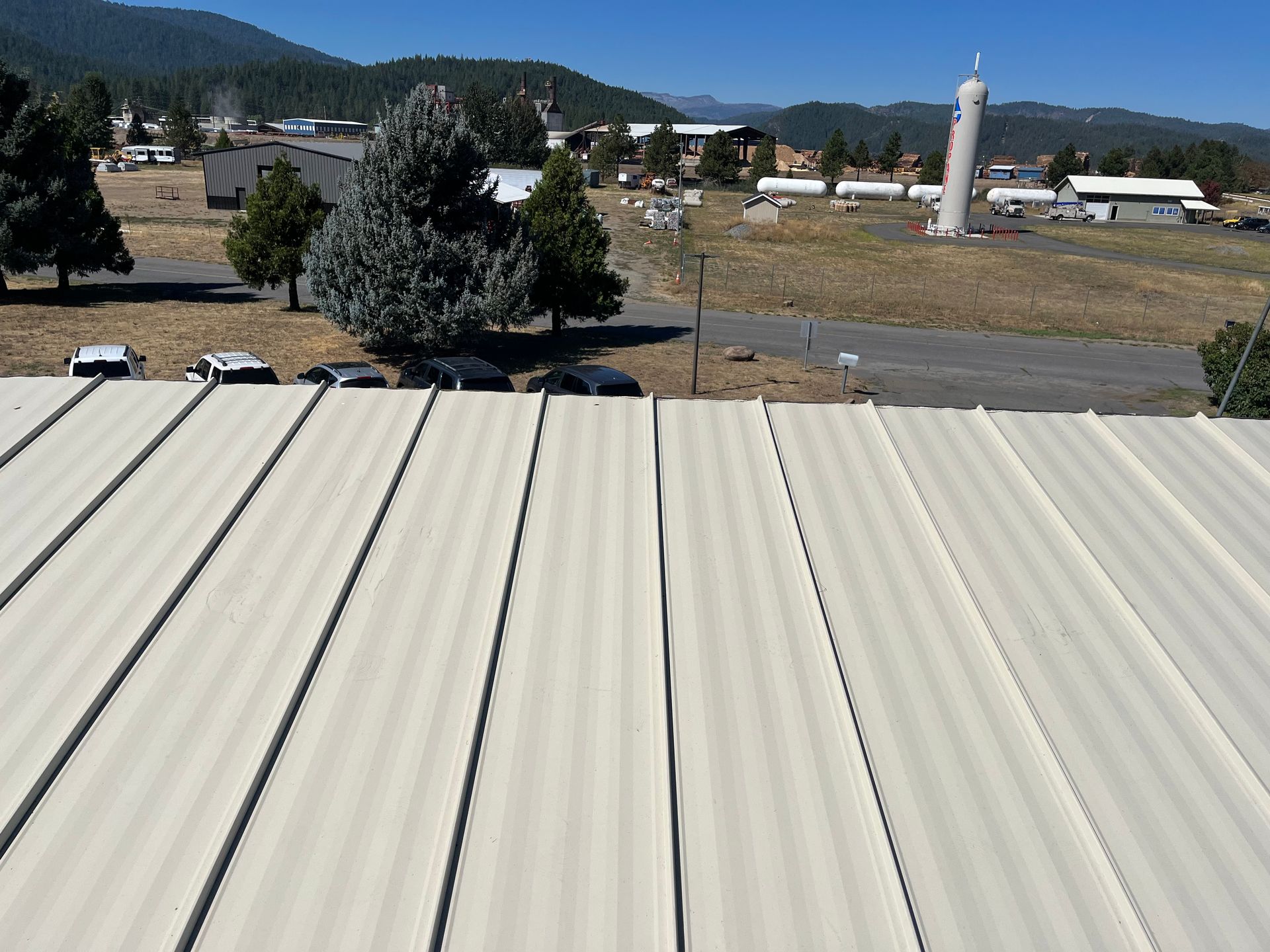 Rural landscape with white metal roof in foreground, trees, buildings, and distant hills under a clear sky