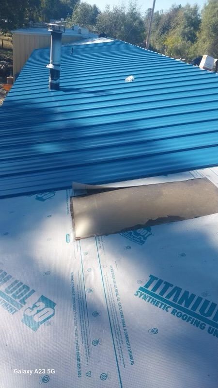 Blue metal roof under construction with white underlayment and rooftop vent pipes