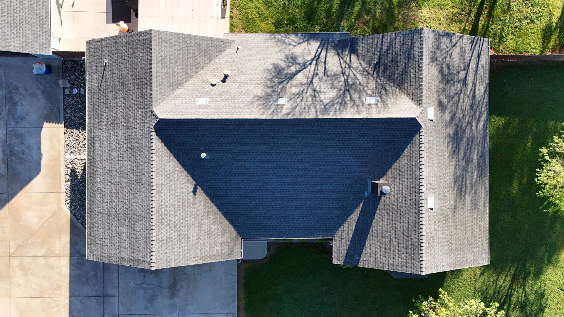Aerial view of a gray-roofed house with a dark triangular driveway and surrounding yard