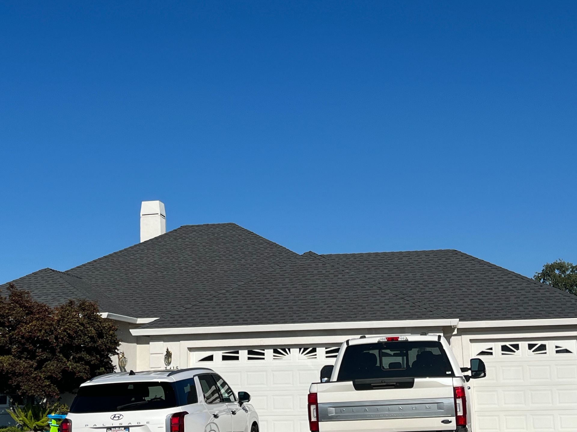 Suburban house with a dark roof and two parked vehicles under a clear blue sky