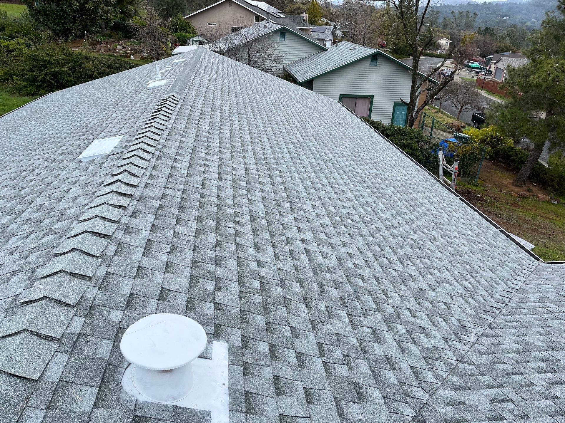 Snow-covered roof with satellite dishes, viewed from above in a residential neighborhood