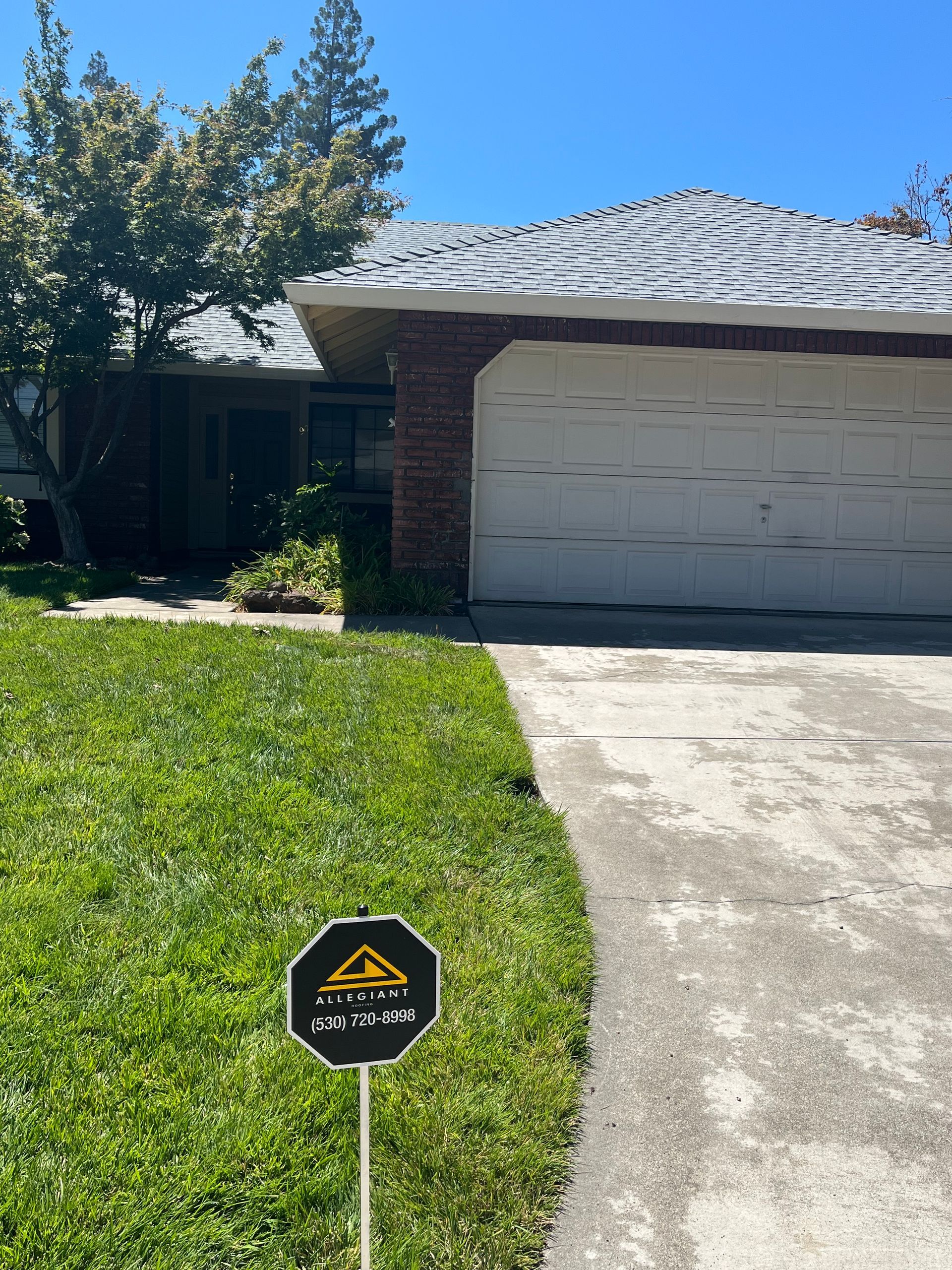 Suburban house with brick garage, sunlit lawn, and a security sign in the front yard.