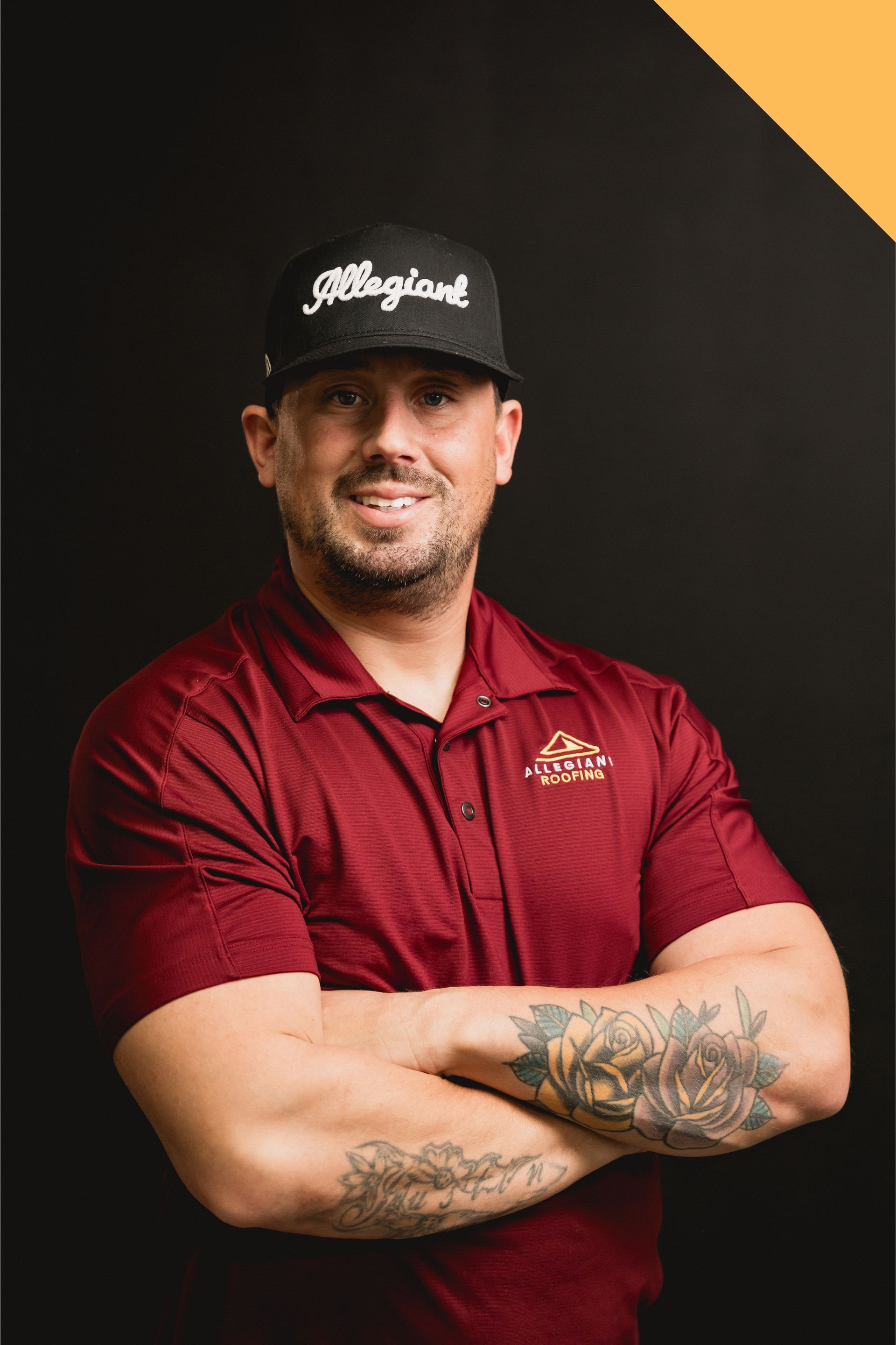 Man in black cap and red polo with crossed arms against a dark background