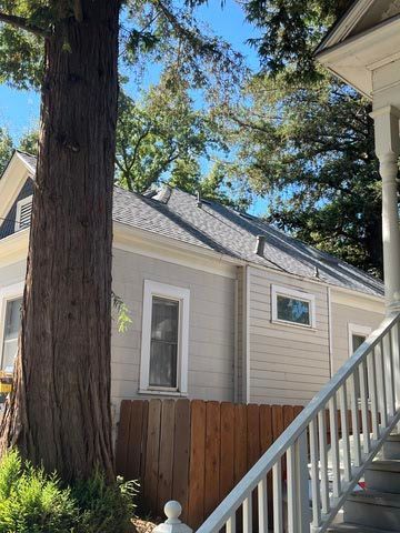 Backyard view of a beige house, tall tree, wooden fence, and outdoor staircase under blue sky