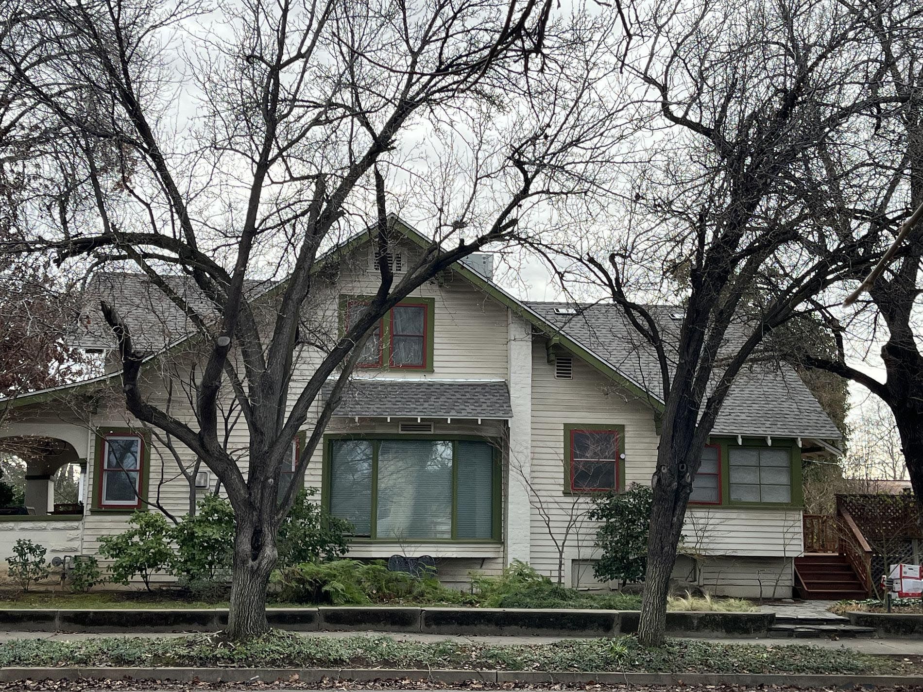 Two-story house with light siding and dark roof, framed by bare trees in a front yard.