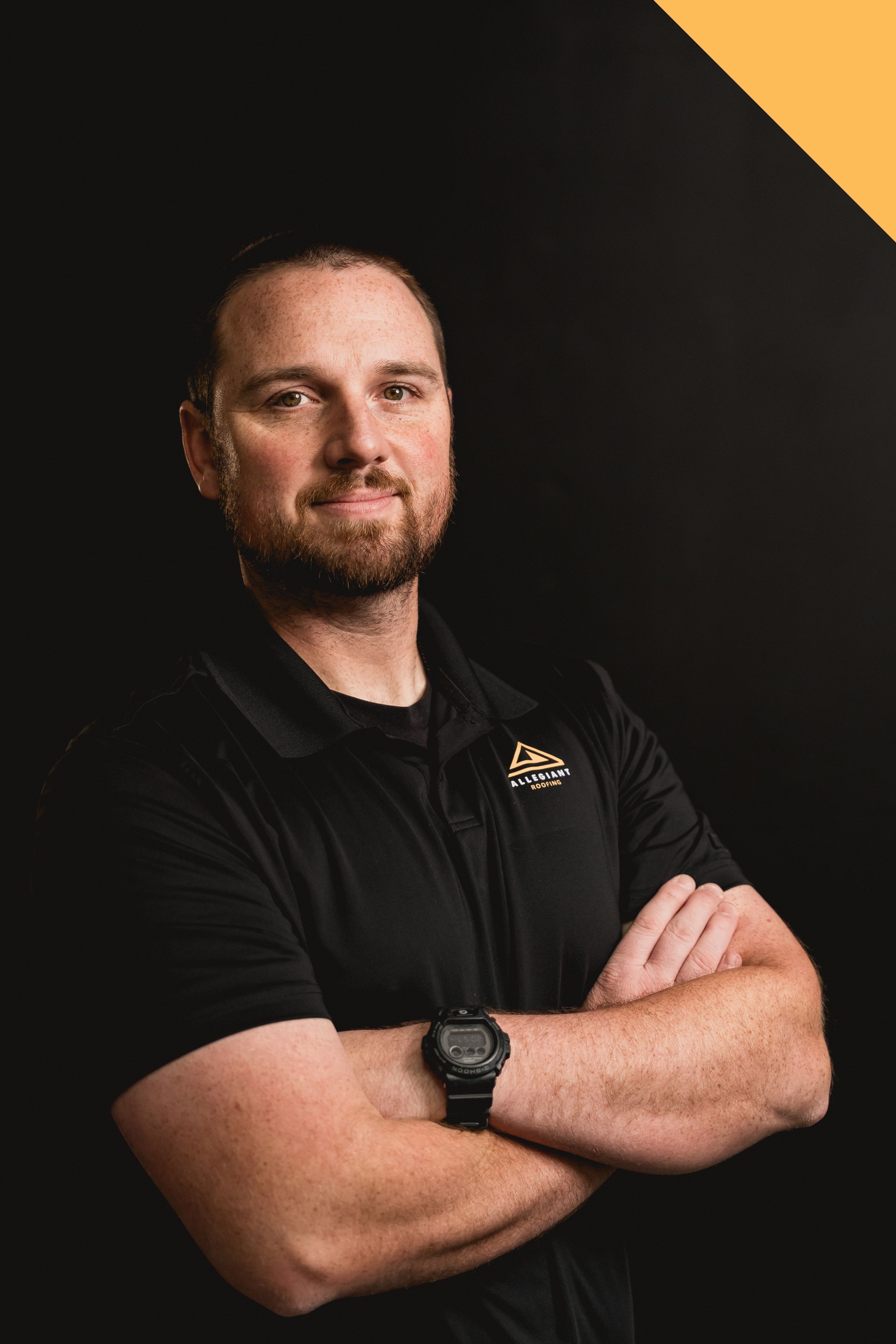 Man with folded arms in black shirt against dark background with gold corner accent
