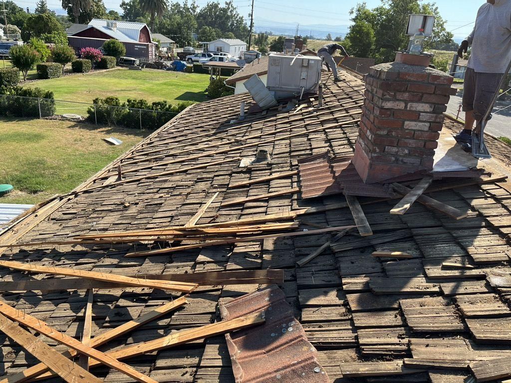 Damaged shingle roof with debris and a brick chimney in a suburban neighborhood