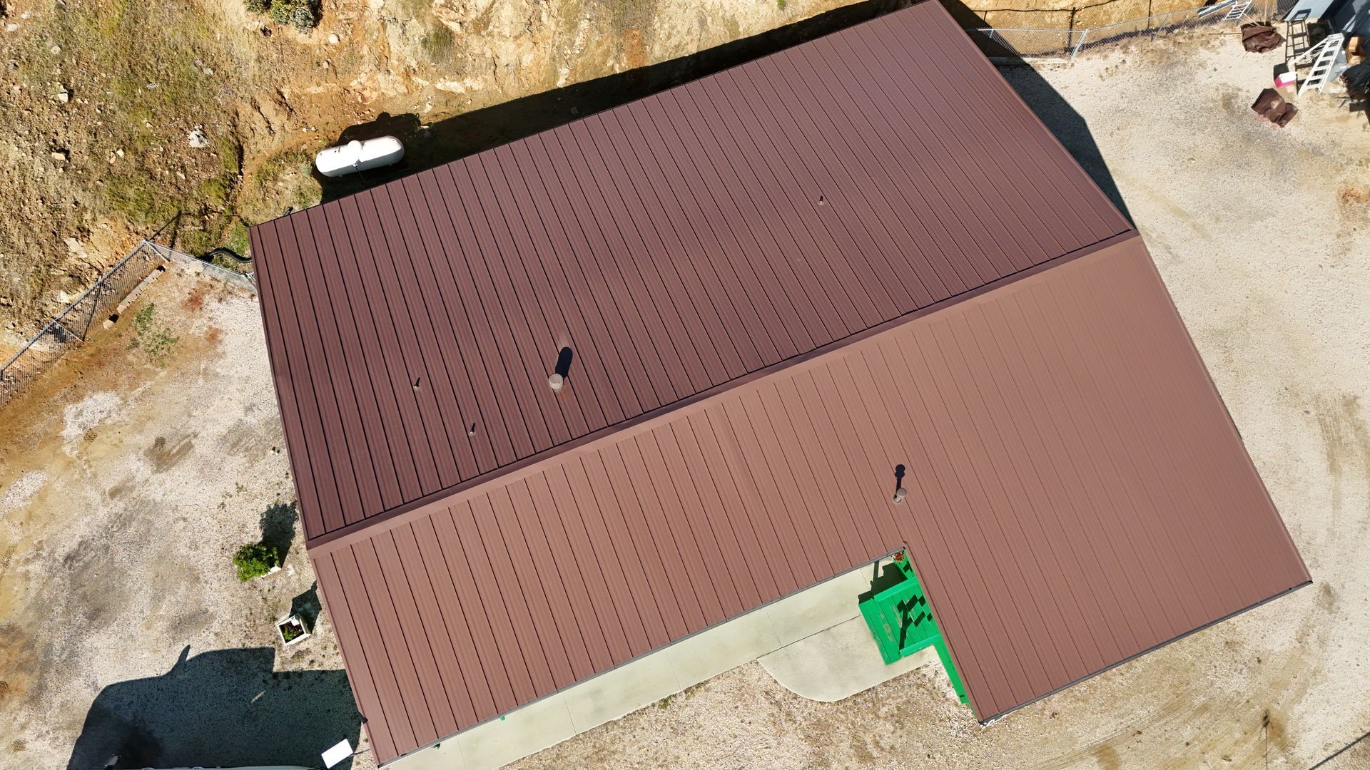 Aerial view of a house with a brown roof and green entryway beside a gravel driveway.