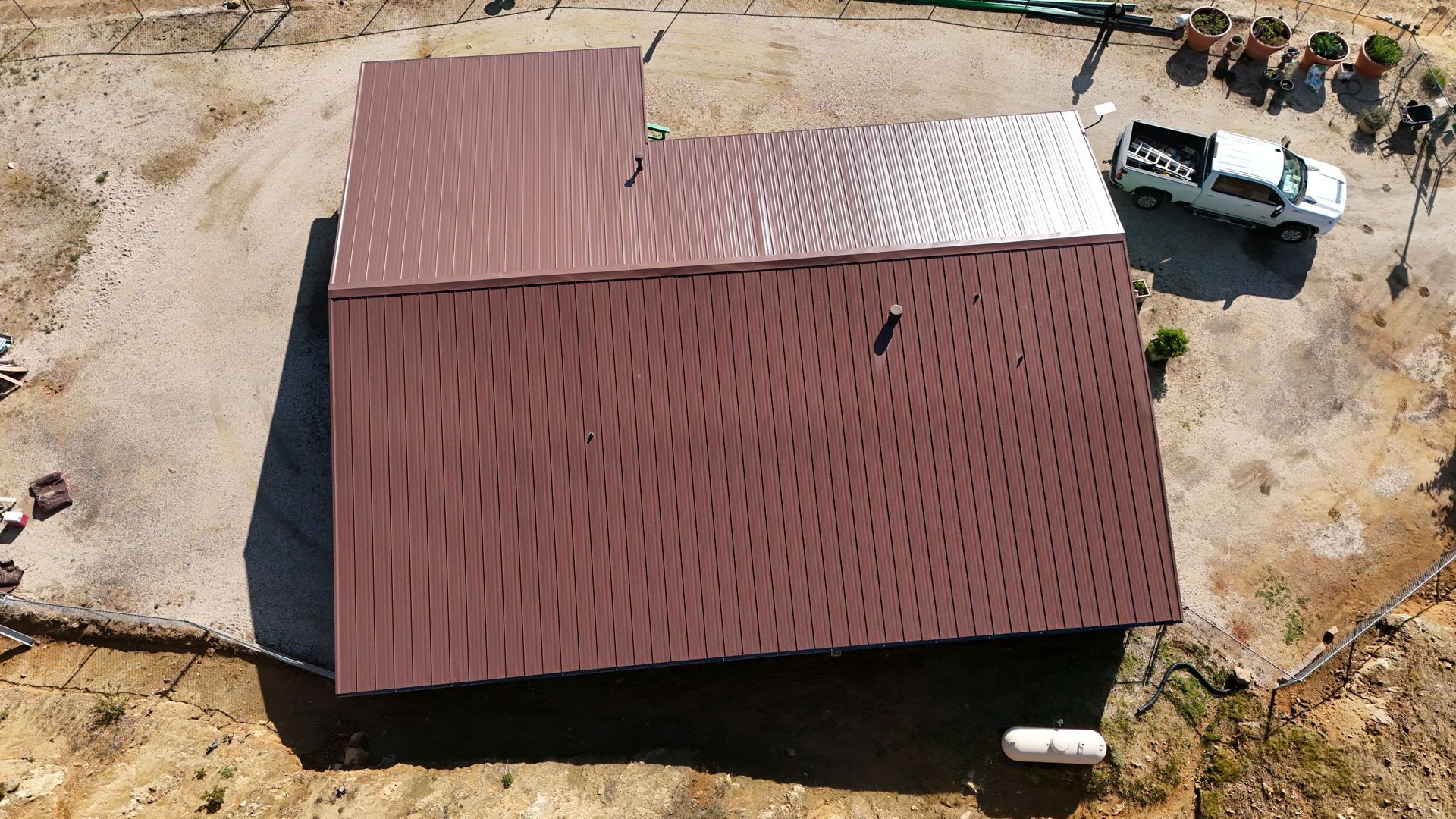 Aerial view of a brown-roofed house beside a white truck on a dirt lot.