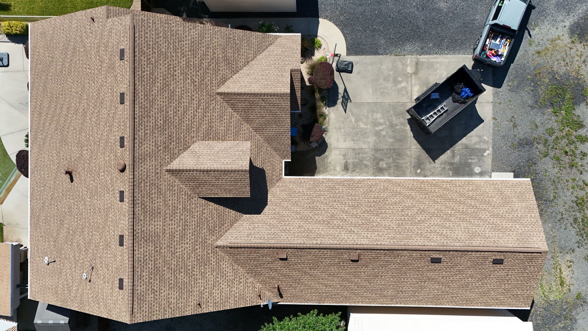 Aerial view of a tan-roofed house beside a driveway with a trash bin and a pickup truck