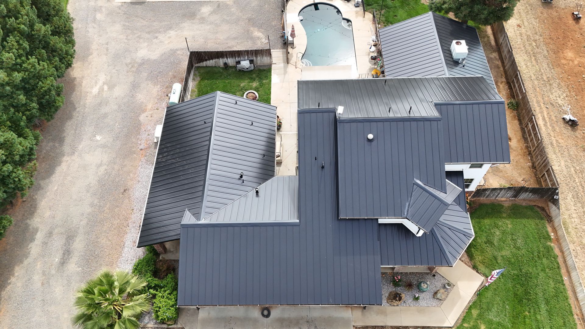 Aerial view of a house with dark roof, driveway, and backyard pool on a rural property.