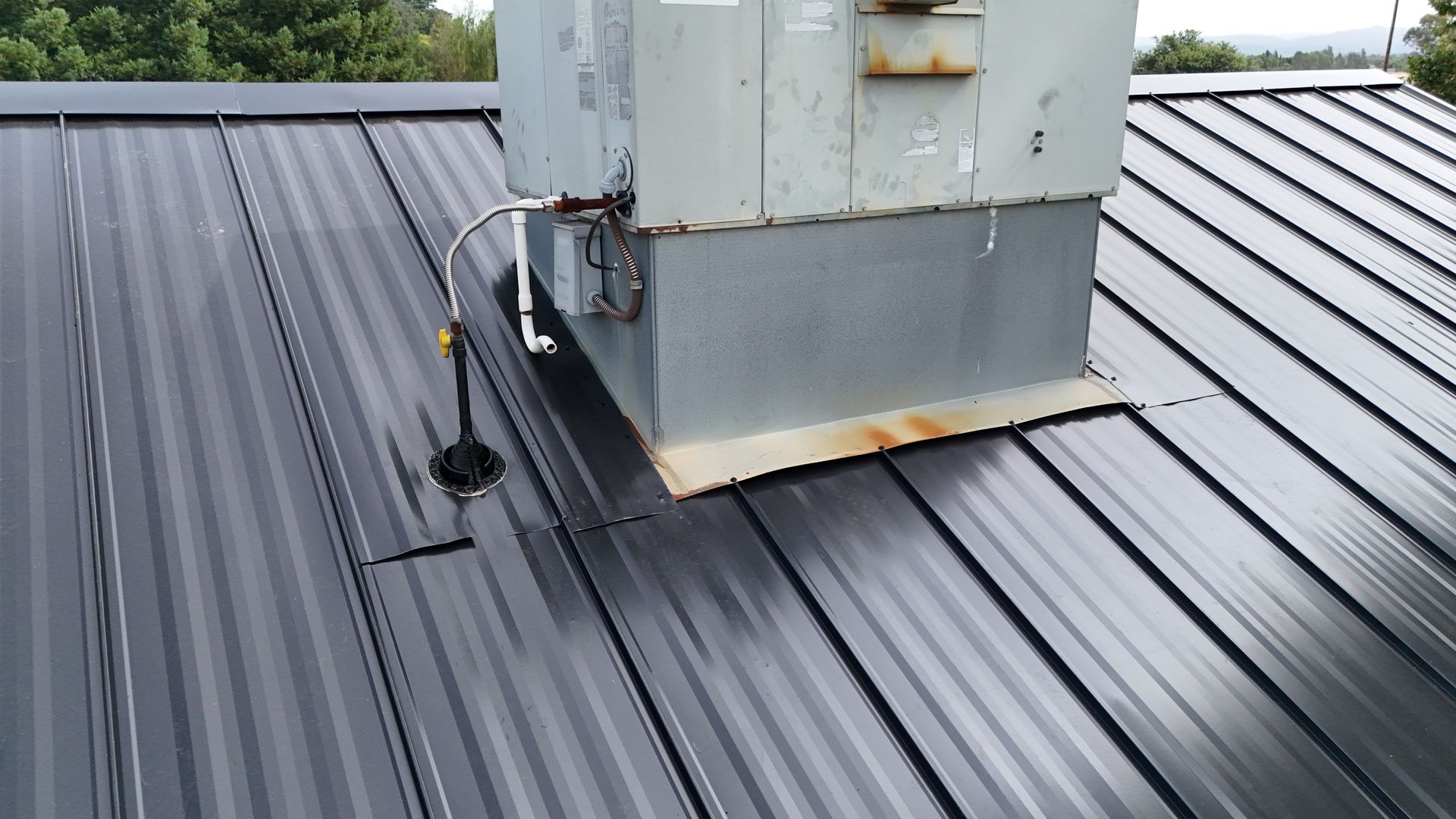 Rooftop HVAC unit on a dark metal roof with a small black antenna nearby