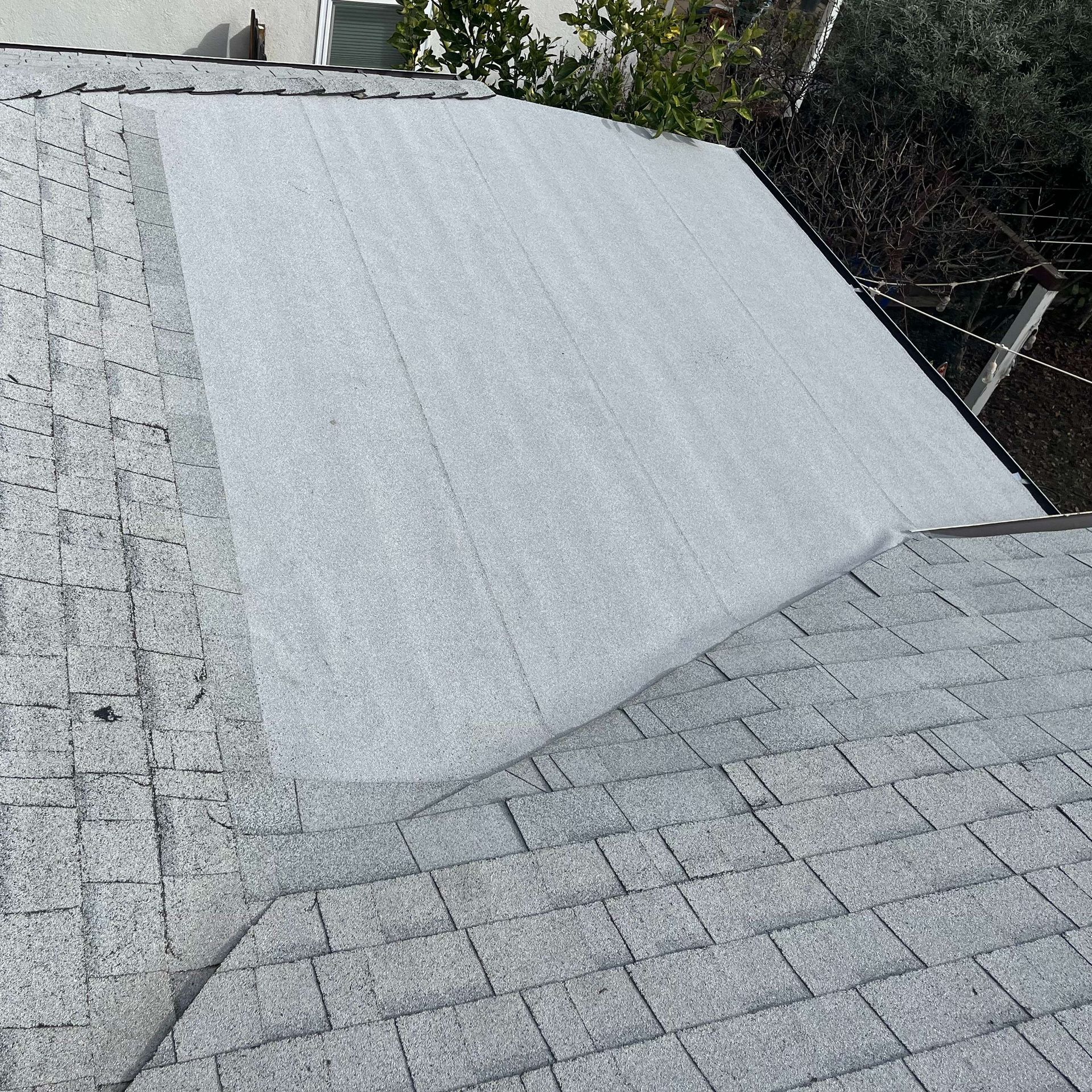 Rooftop with gray shingles and a large white tarp or patch covering part of the roof.