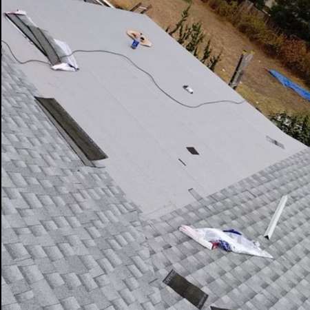 Rooftop under repair with gray roofing material, vents, and scattered tools on a sloped shingles roof.