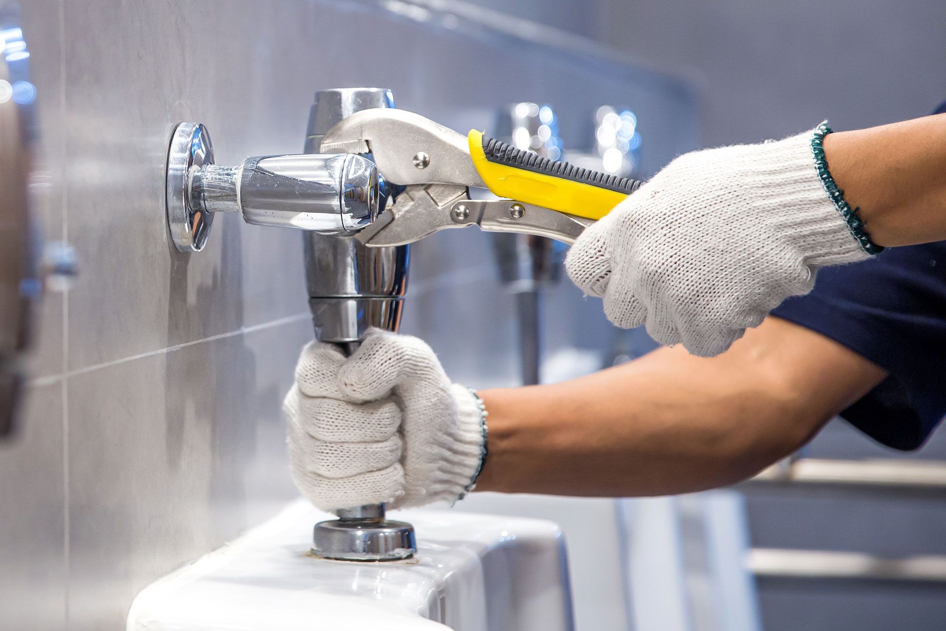 Gloved worker tightening a faucet with a wrench on a stainless steel sink.