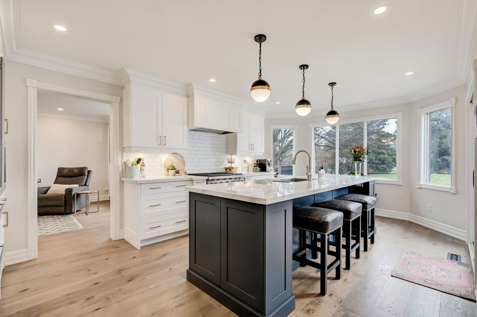 Bright white kitchen with black island, pendant lights, bar stools, and open doorway to living room