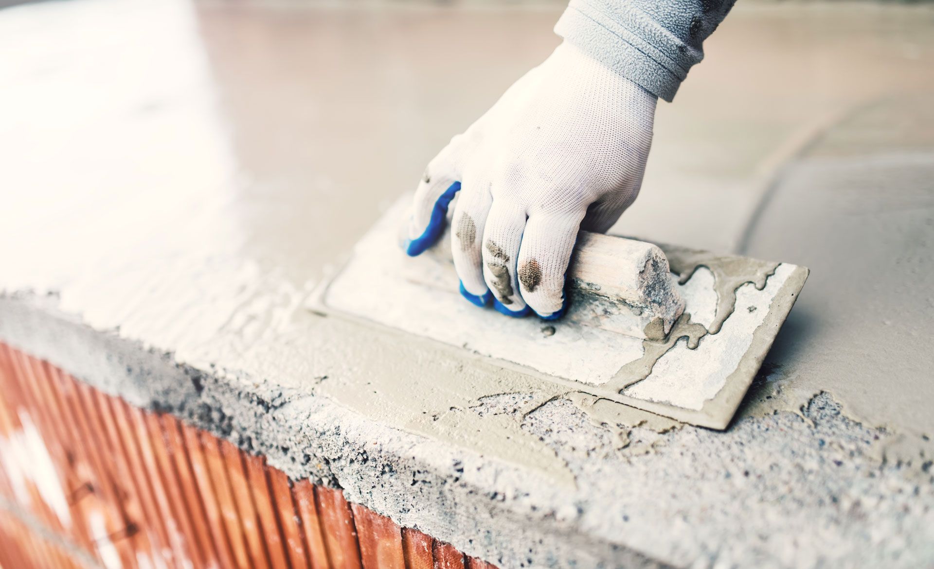 Gloved hand smoothing wet concrete with a trowel on a brick ledge