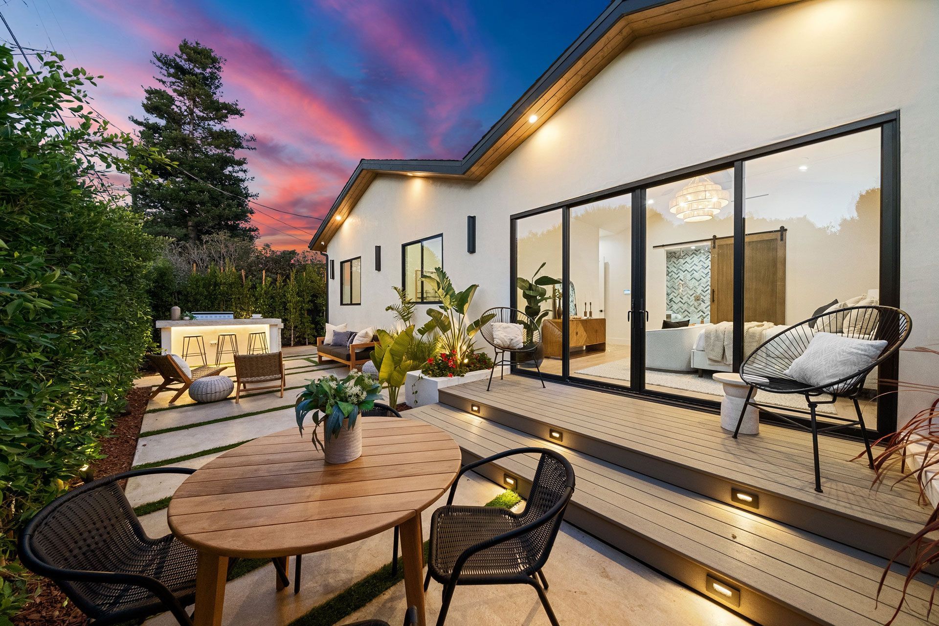 Outdoor patio with round table, chairs, and lounge seating beside a modern home at sunset
