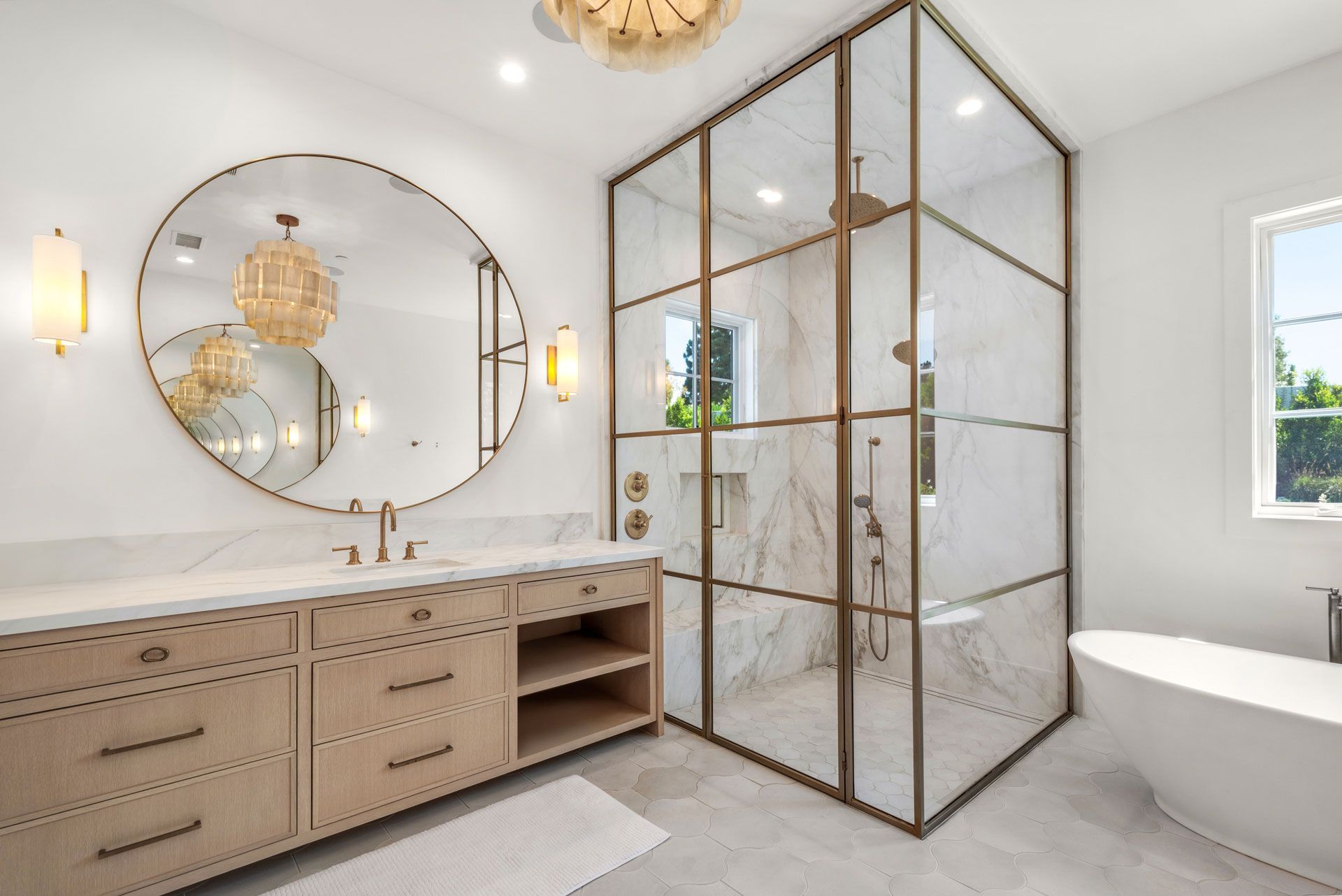 Bright modern bathroom with marble vanity, round mirror, glass shower, and freestanding tub