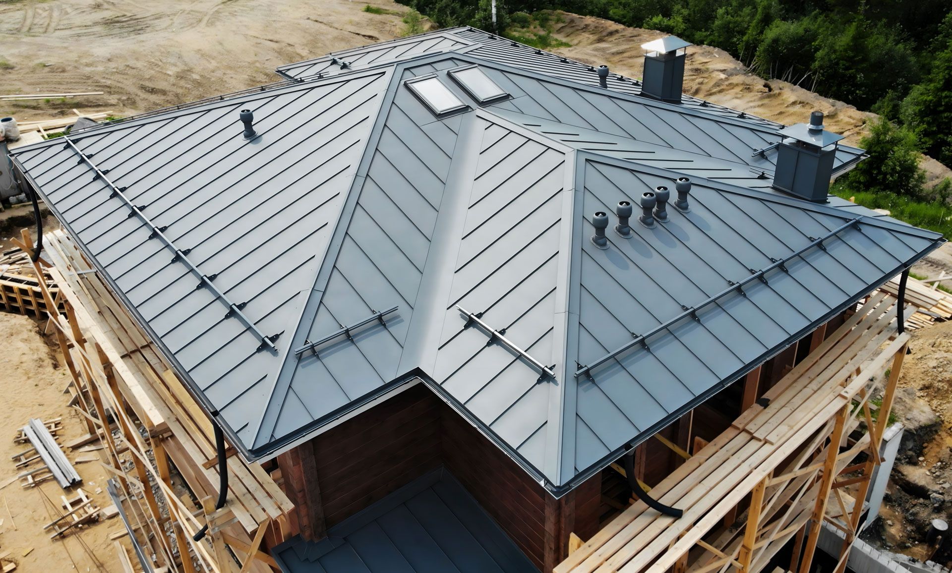 Aerial view of a house with a gray metal roof under construction, surrounded by wooden scaffolding.
