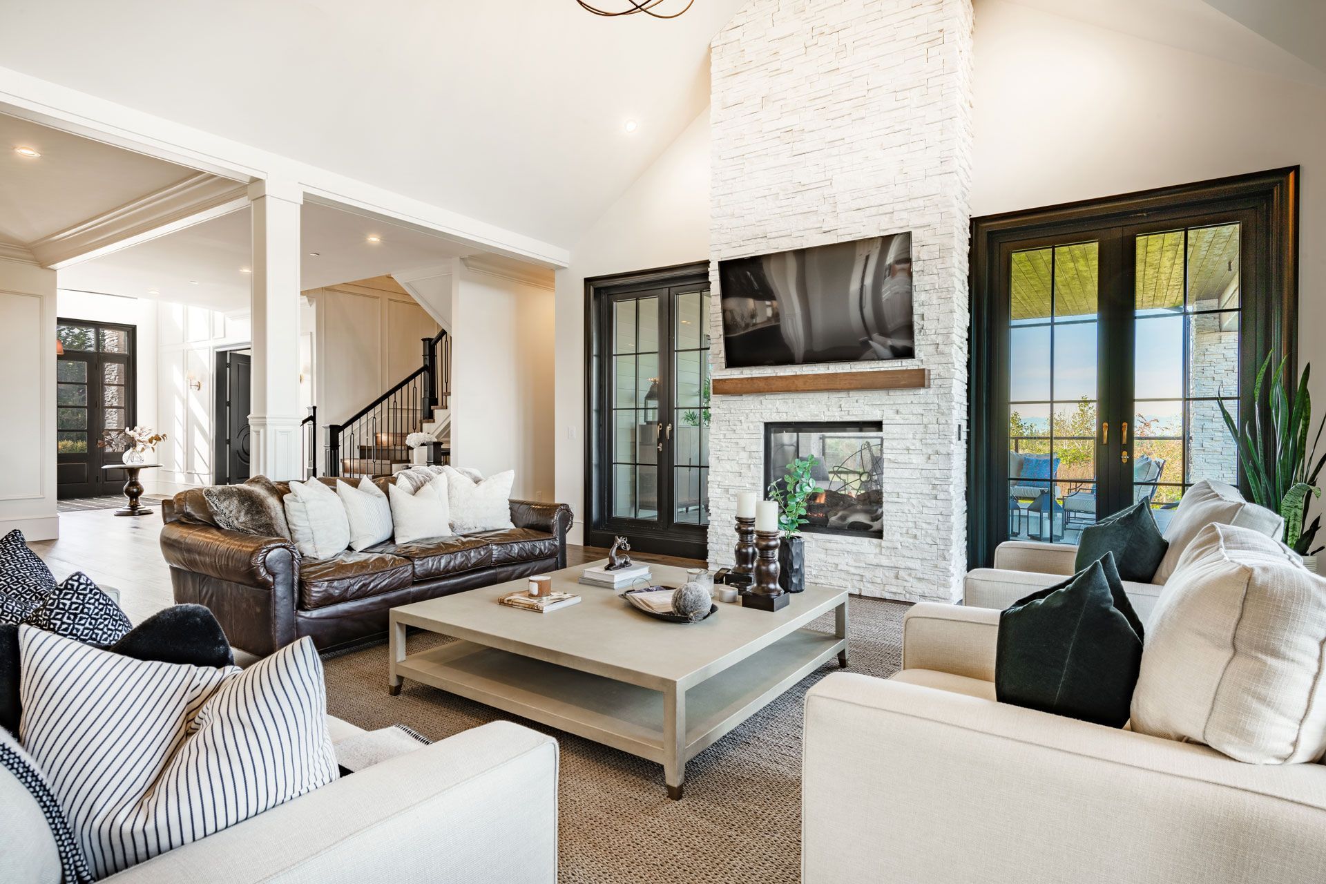 Bright modern living room with white sofas, a large coffee table, fireplace, and dark-framed windows.