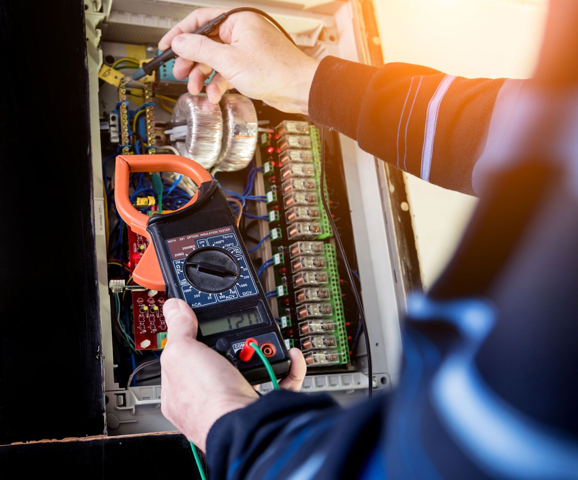 Technician testing electrical panel with multimeter and clear jar, wires and breakers visible