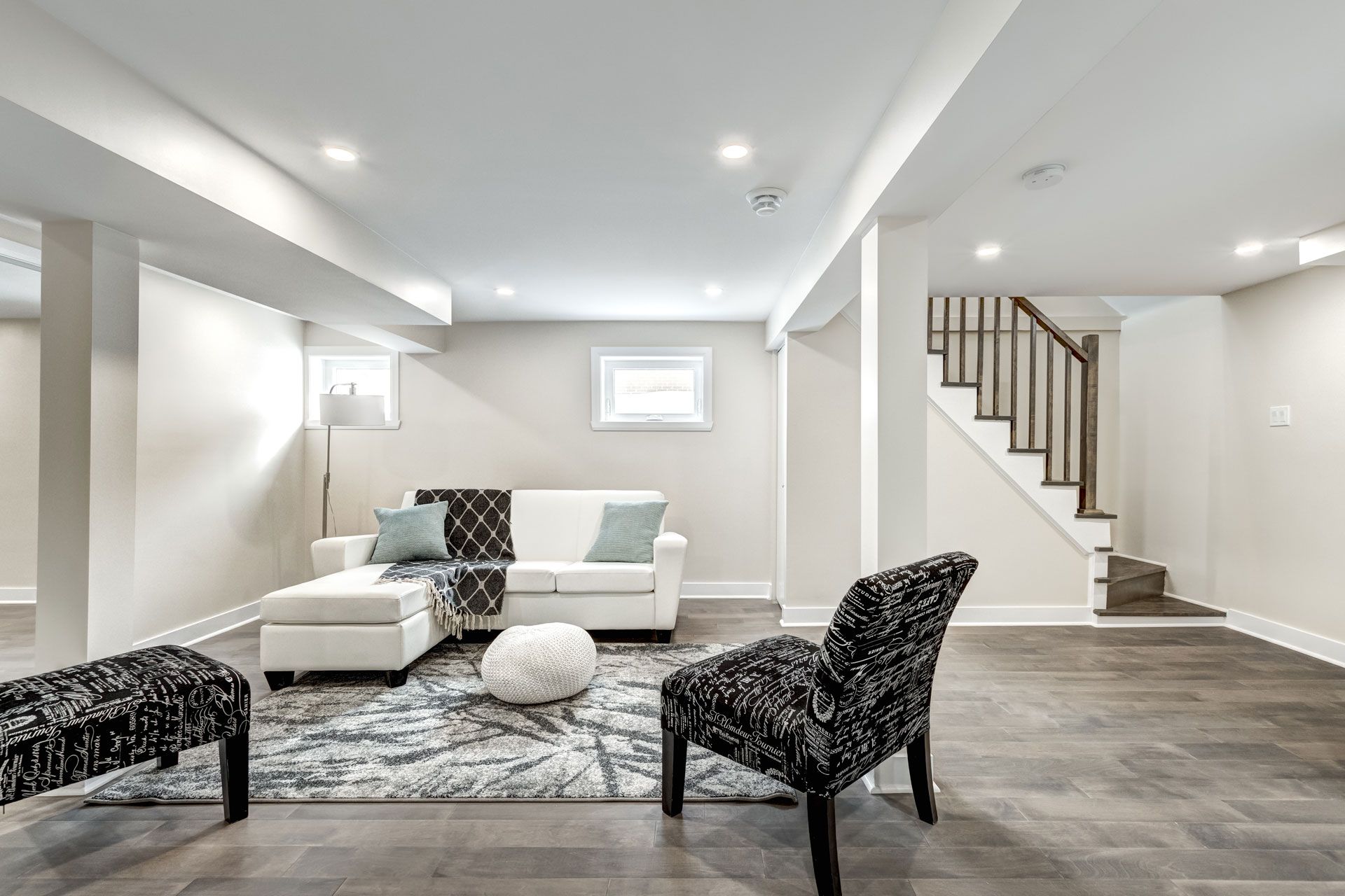 Bright modern living room with white sectional, patterned chairs, gray rug, and staircase on the right