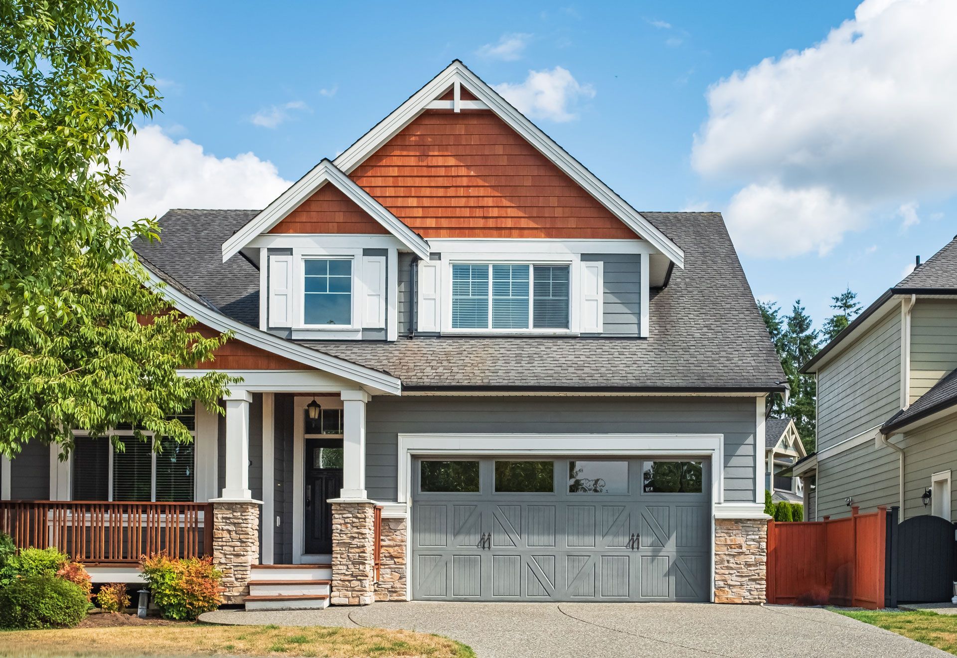 Suburban house with gray garage and red cedar gable, front porch, and blue sky