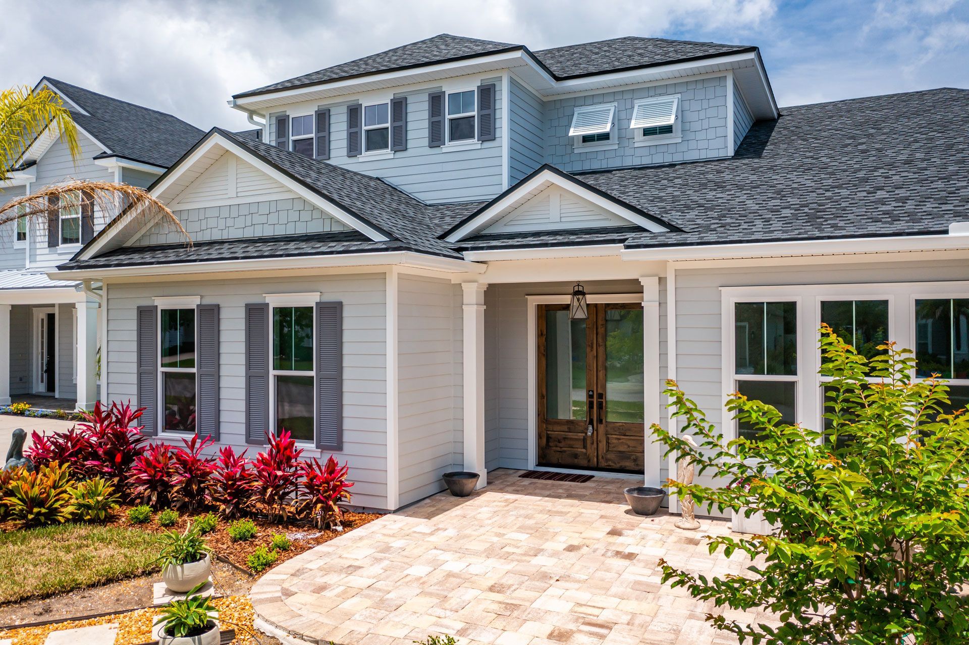 Modern two-story house exterior with white siding, gray roof, stone walkway, and colorful landscaping