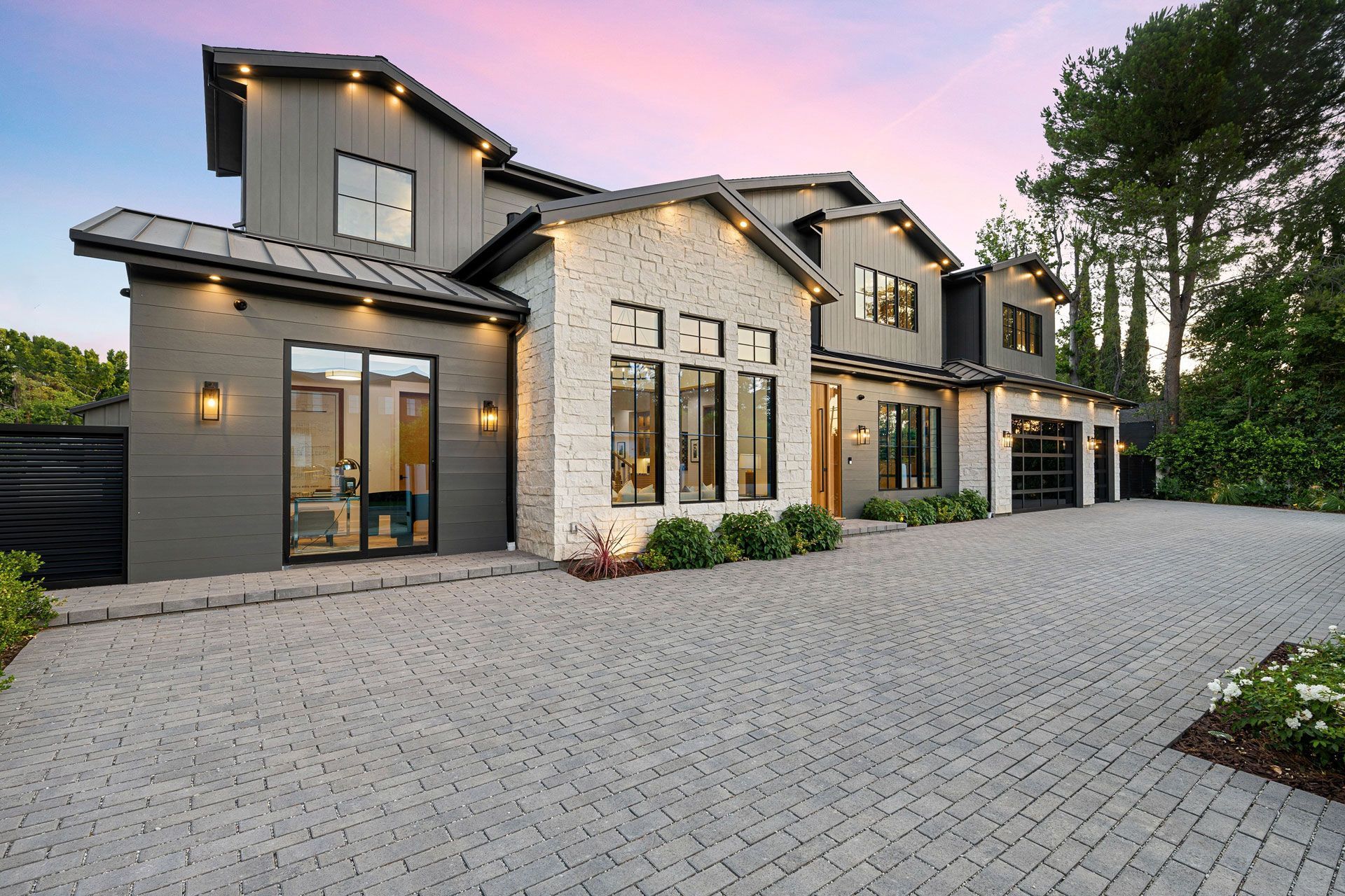 Modern gray two-story house with stone accents and a paved driveway at dusk