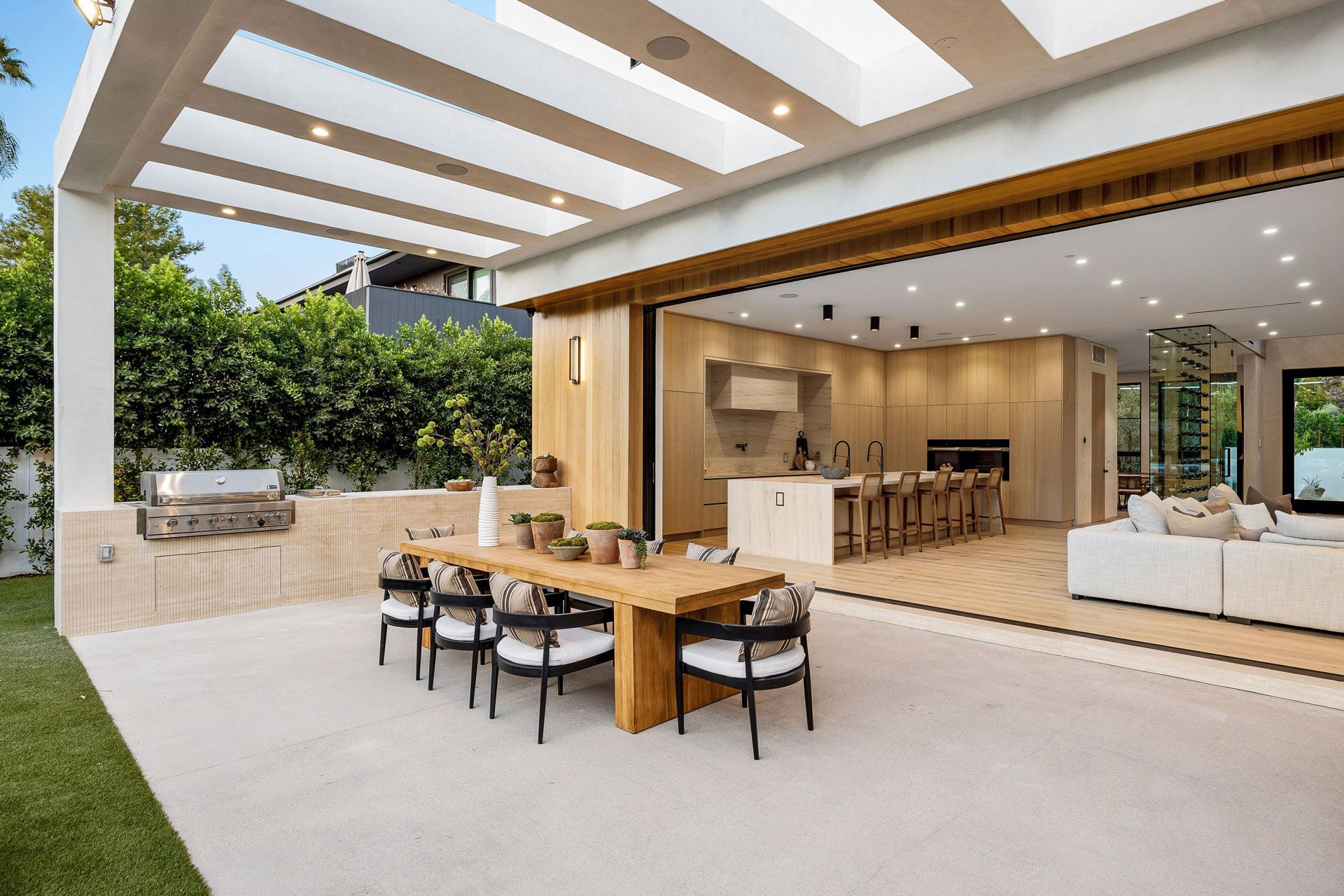 Modern patio with dining table, lounge seating, and open indoor-outdoor living space under a skylit roof