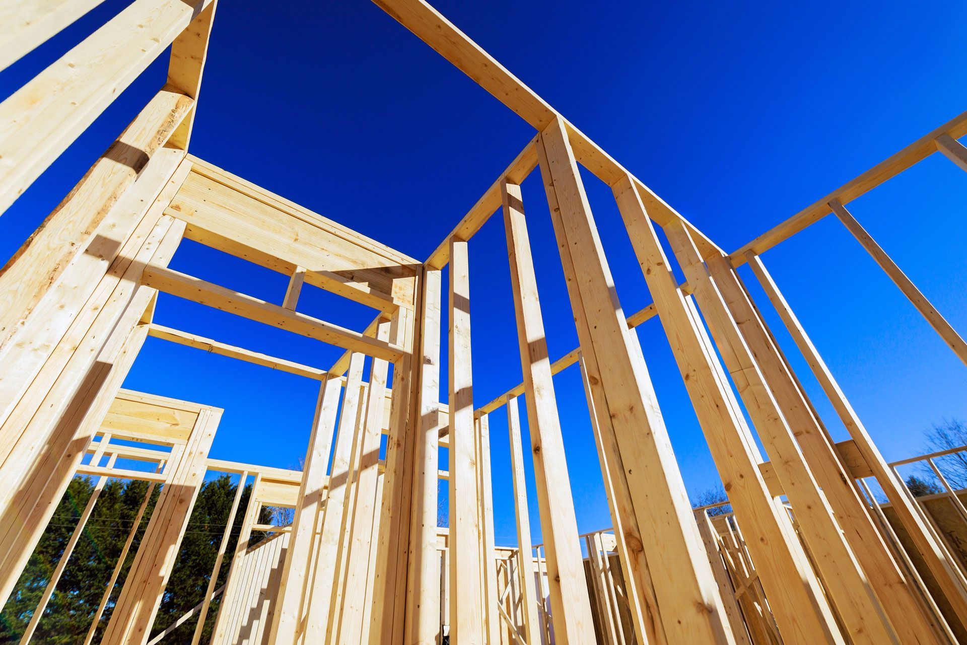 Wooden house framing under construction against a clear blue sky