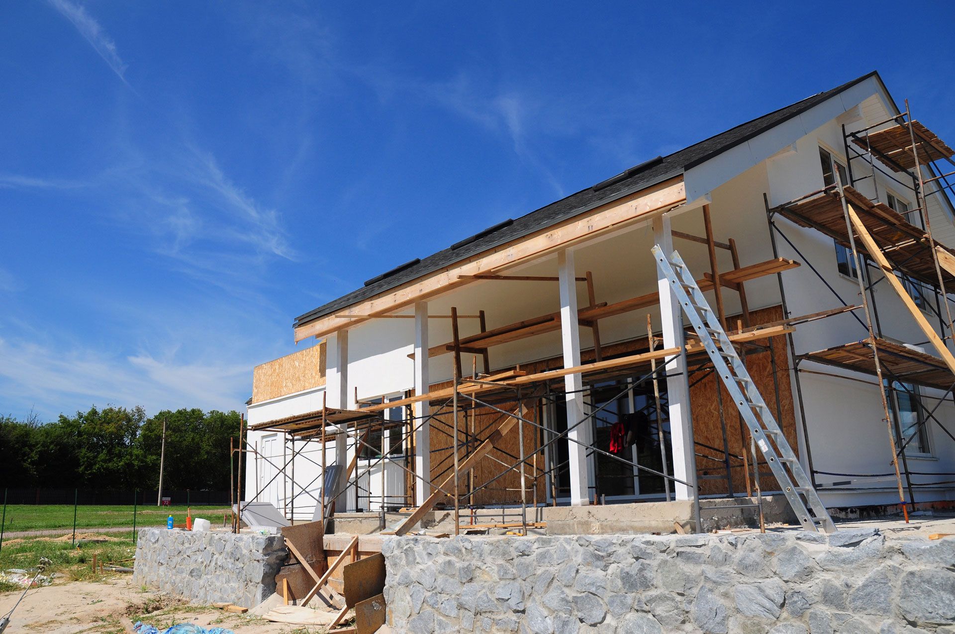 Partially built house with scaffolding and stone foundation under a blue sky
