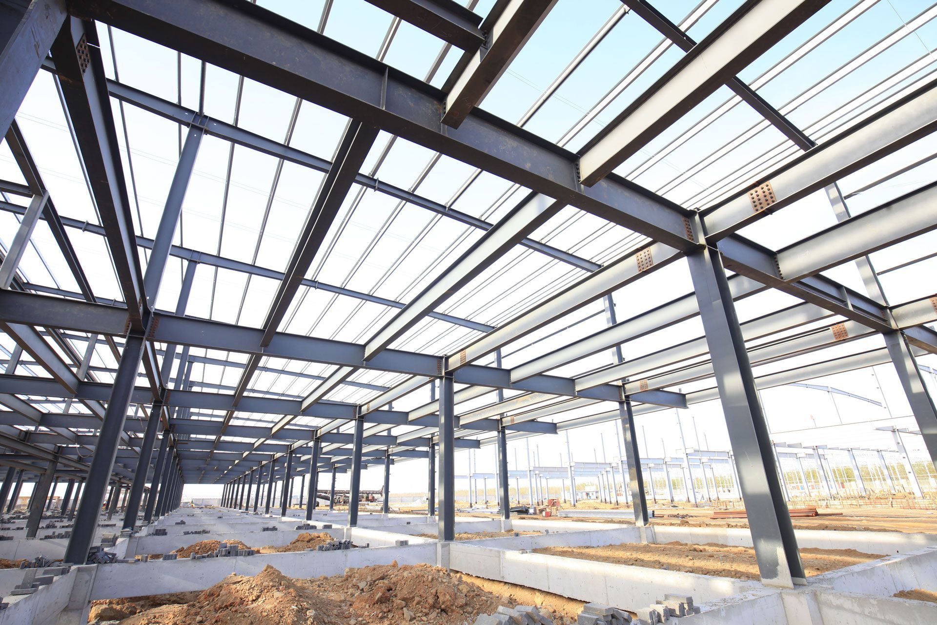 Steel framework of a large building under construction with exposed roof beams and bright daylight.