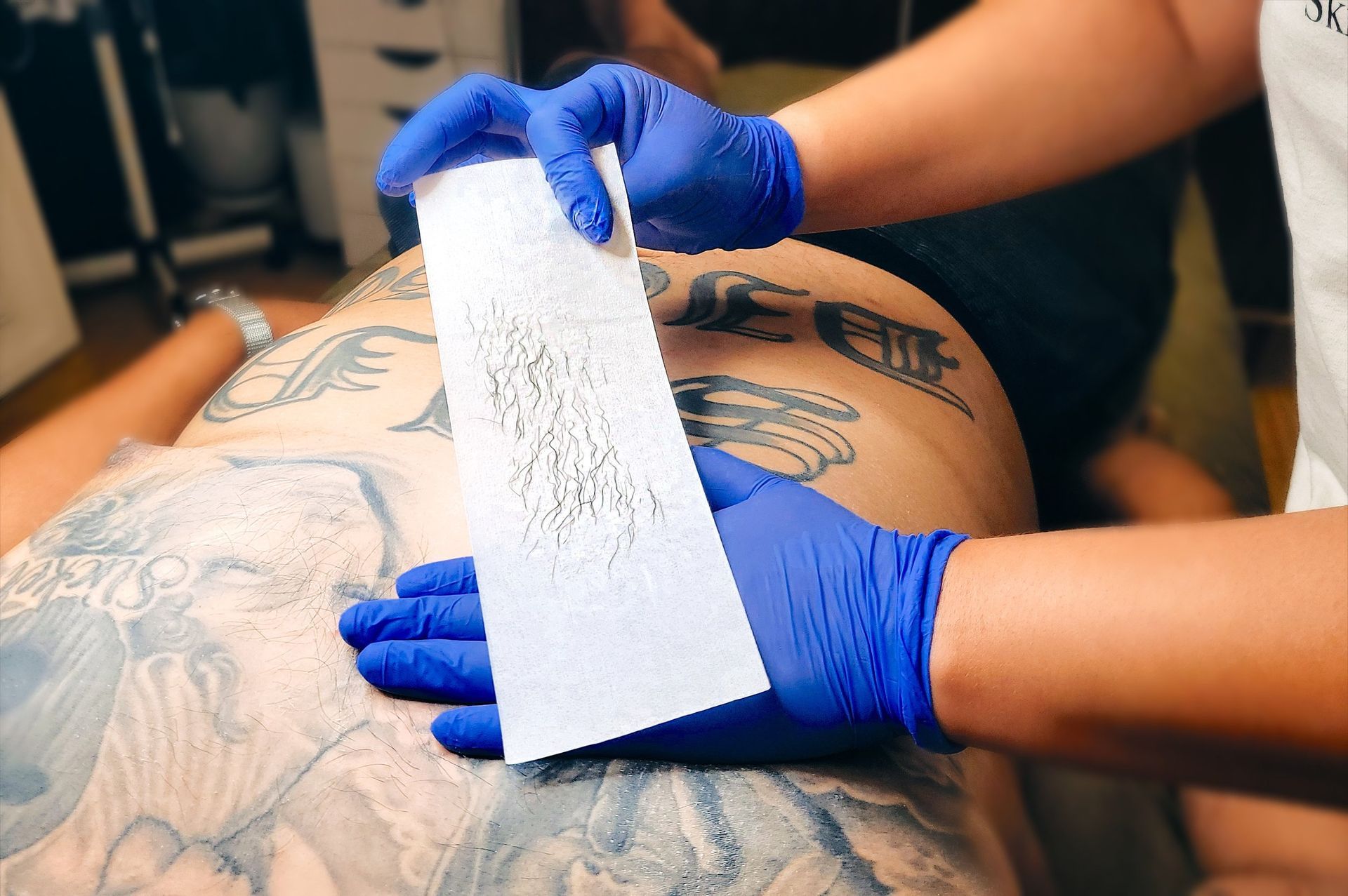 A woman is waxing a man 's back with blue gloves.