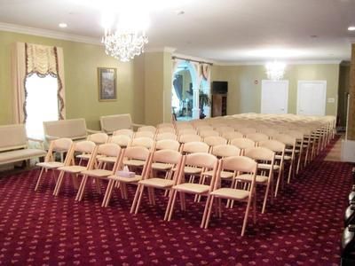 Empty banquet room with rows of beige chairs on a red patterned carpet and chandeliers overhead