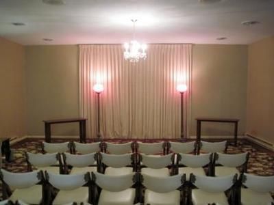 Small banquet hall with rows of white chairs facing a curtained wall and two lit wall sconces.