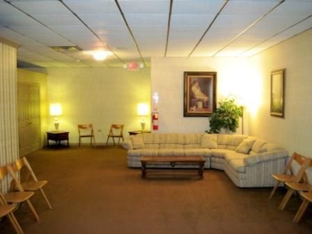 Dim waiting room with beige couches, chairs, framed art, and a small table under warm lighting