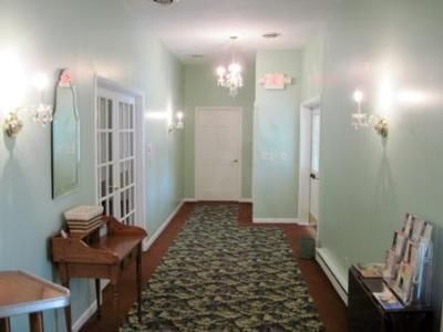 Long narrow hallway with pale green walls, patterned carpet, wall sconces, and a small desk on the left.